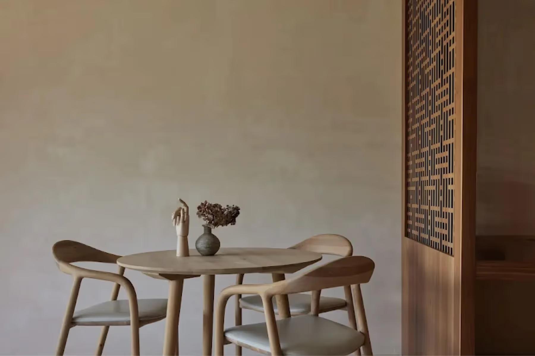 Minimal dining table with two wooden chairs beside an informational board on neutral walls