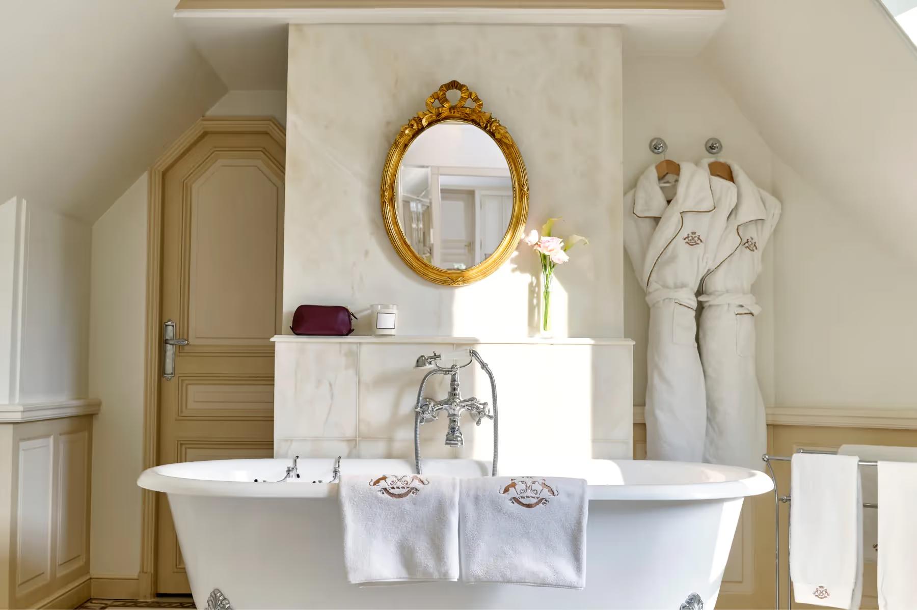 A bathroom with freestanding white marble tub and gilt-framed mirror and classical details