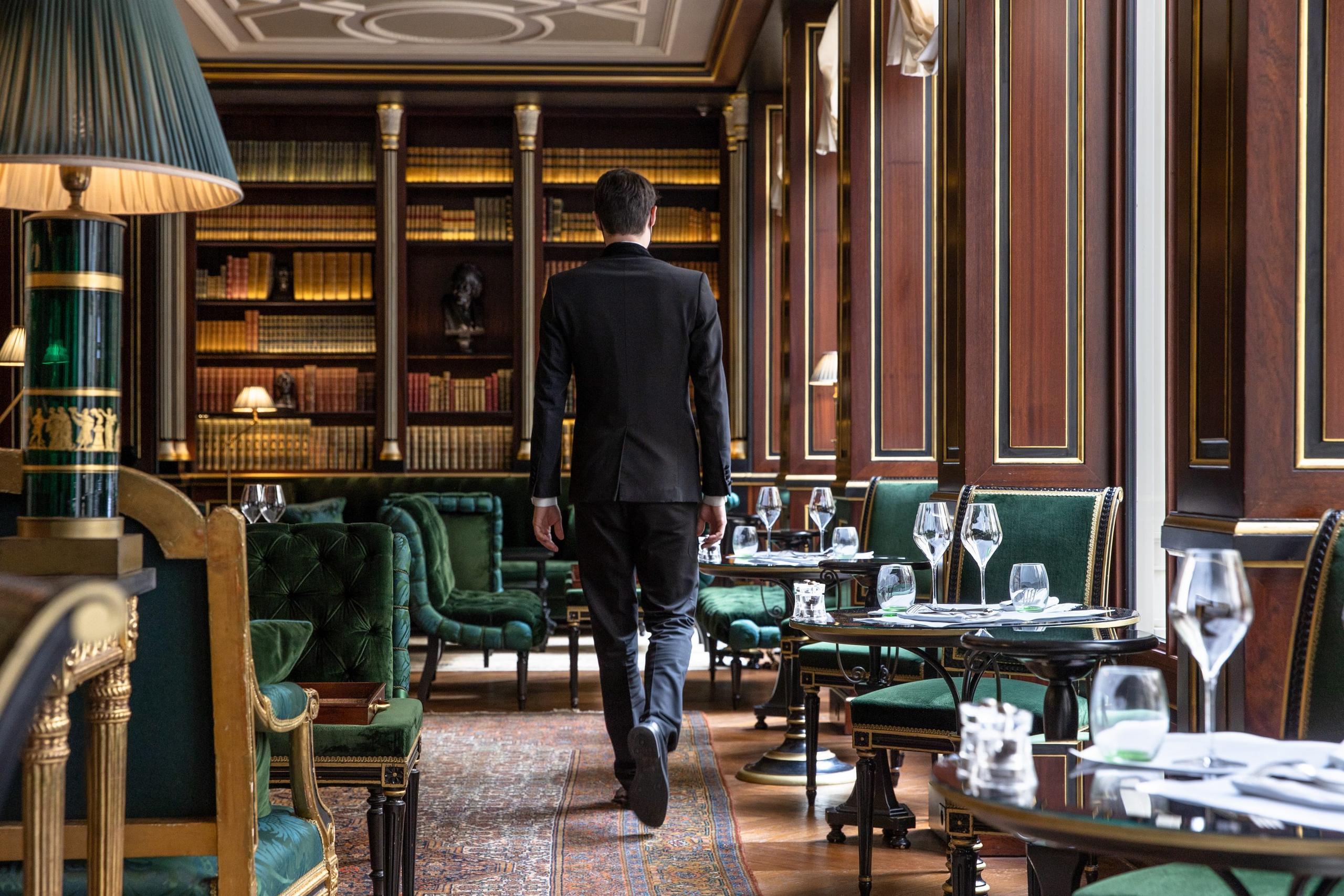 The dining room with dark wood walls, green furniture, and gilded library shelving