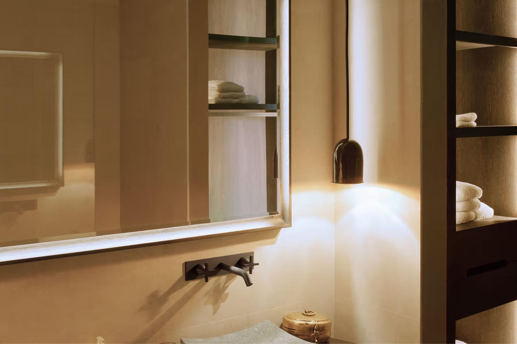 Modern vanity with illuminated mirror and built-in shelving in earth-toned room