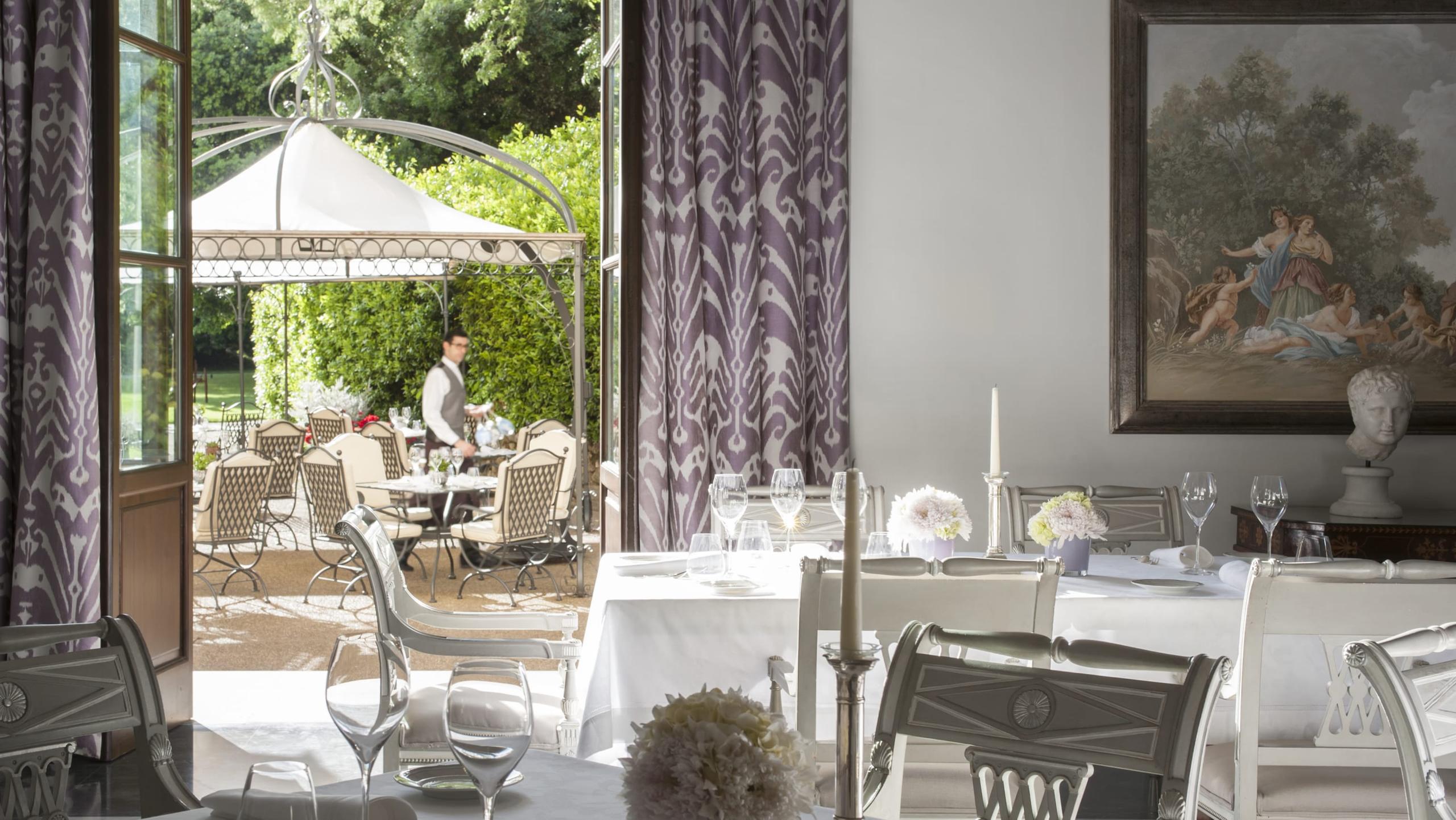 Restaurant terrace overlooking gardens with white tablecloth settings and purple drapery