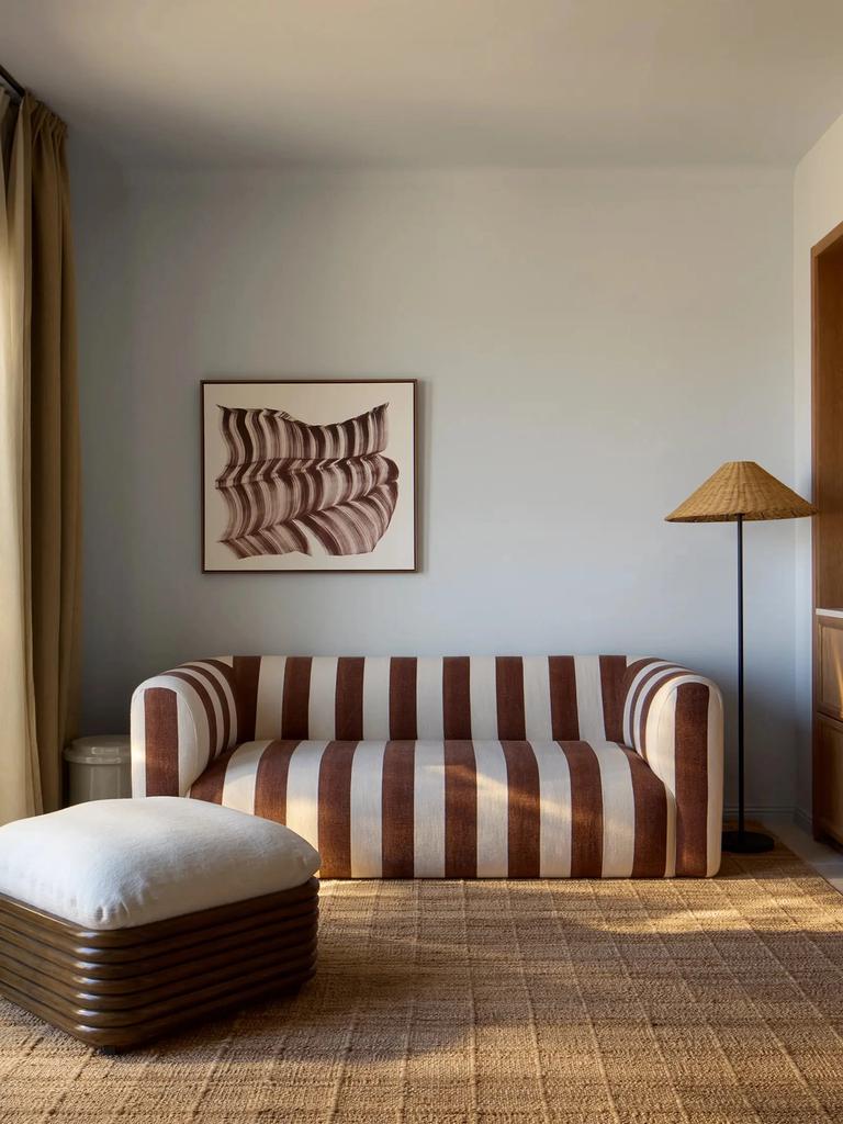 A Delos room with a brown and white striped sofa, a woven rug and a cane lampshade