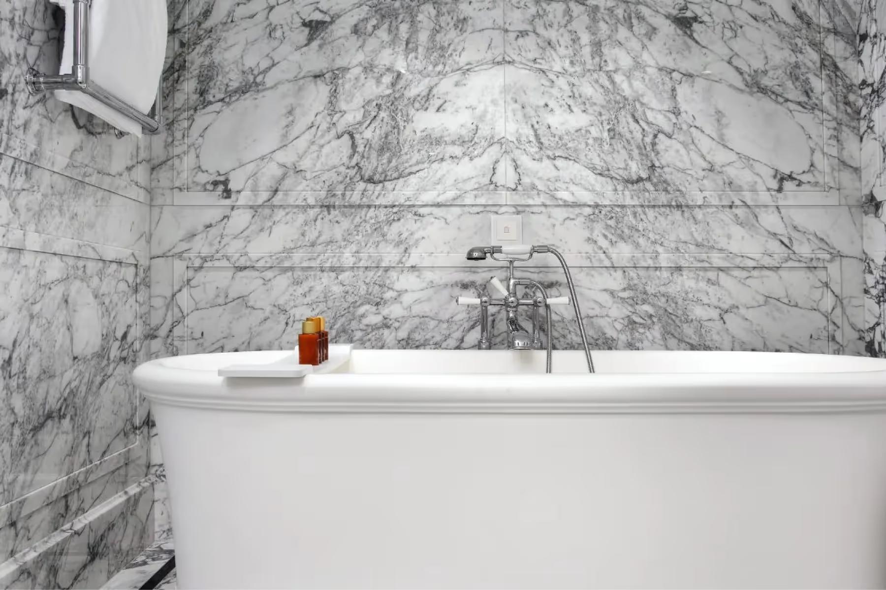 Marble bathtub surrounded by white marble walls with brass fixtures
