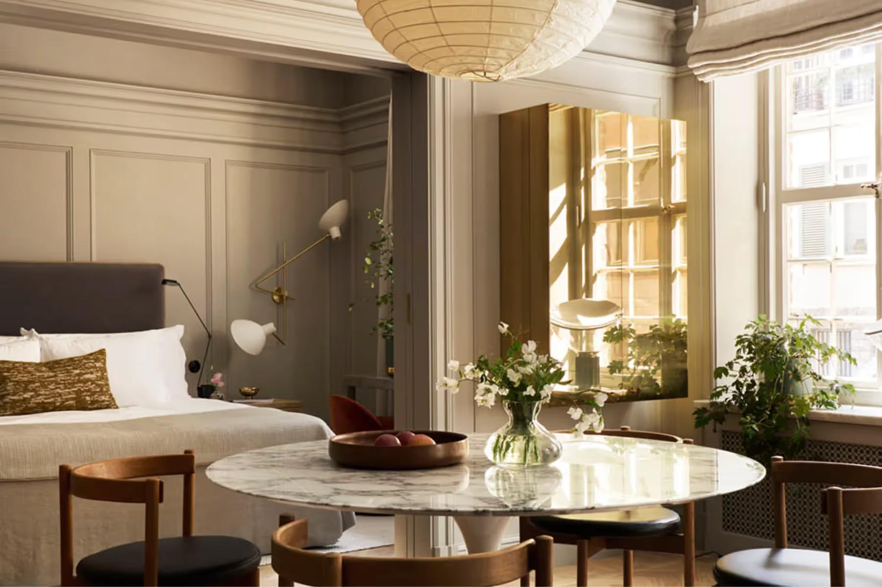Ett Hem: a bedroom with dark headboard, cream bedding, round glass side table, and tall windows with natural light