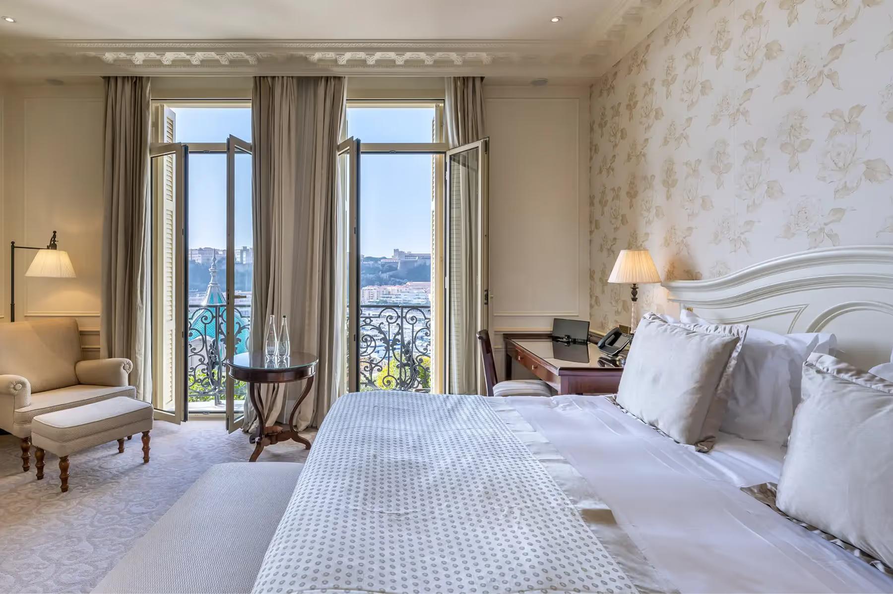 Suite bedroom with sea views through double doors, white bed and neutral furnishings