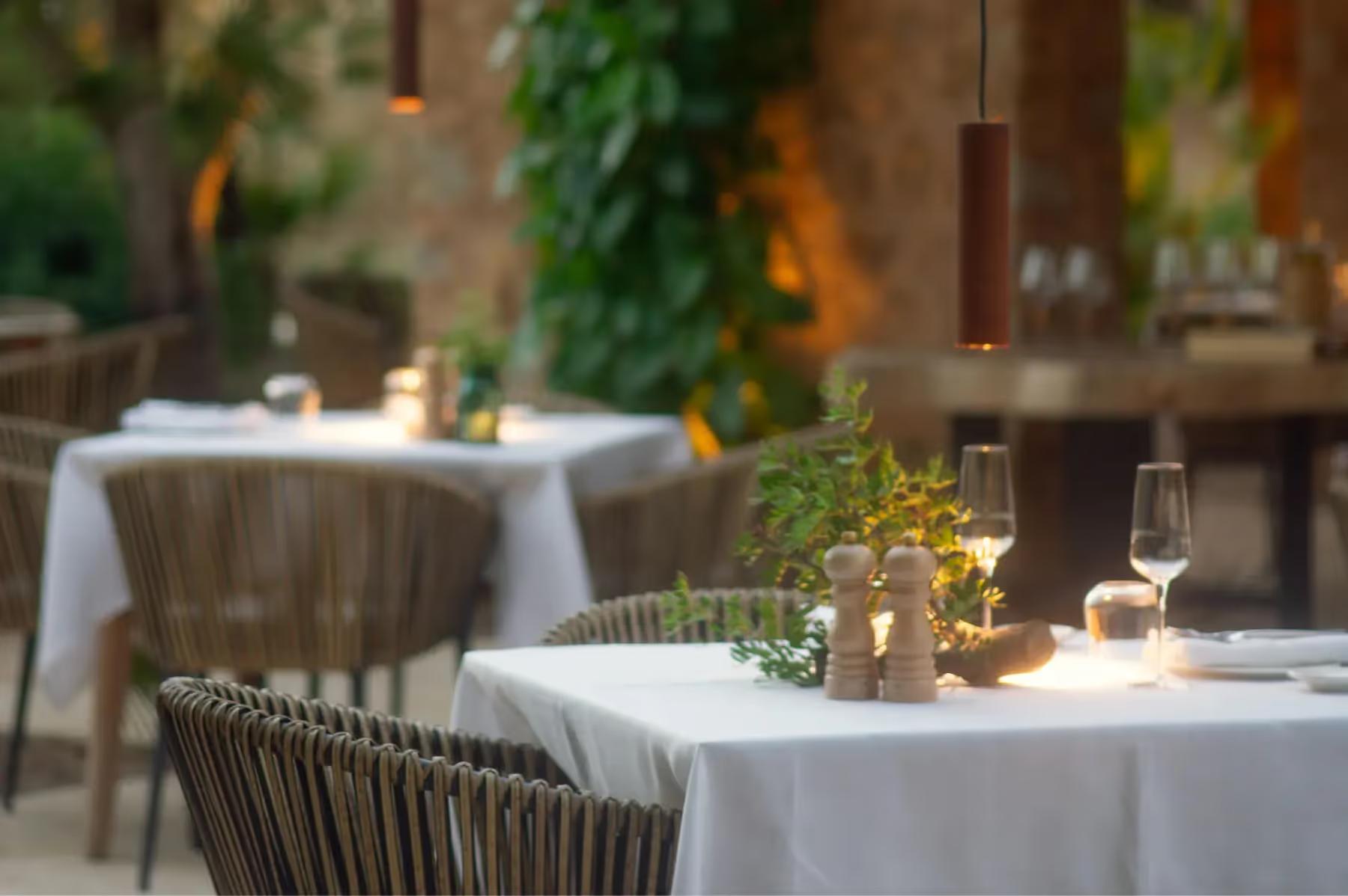 Es Racó d’Artà: two restaurant tables with white linens in a courtyard with stone walls and lush greenery