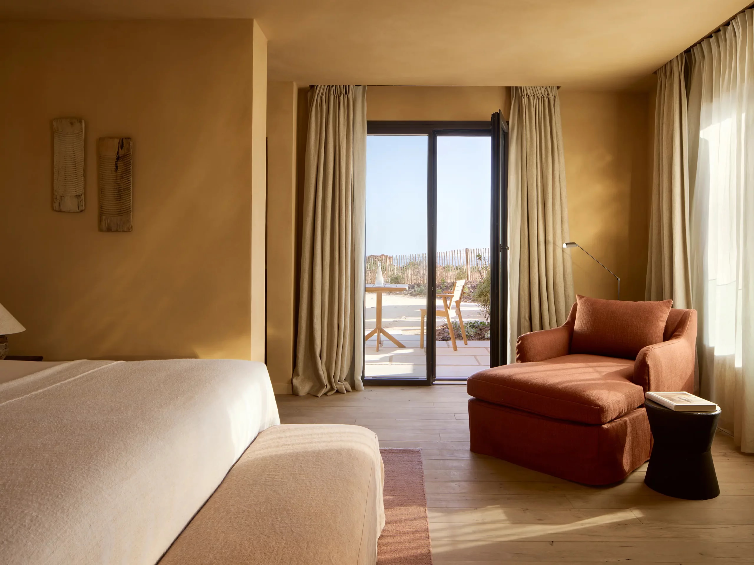A sunlit bedroom opens through glass doors onto a private terrace facing the dunes