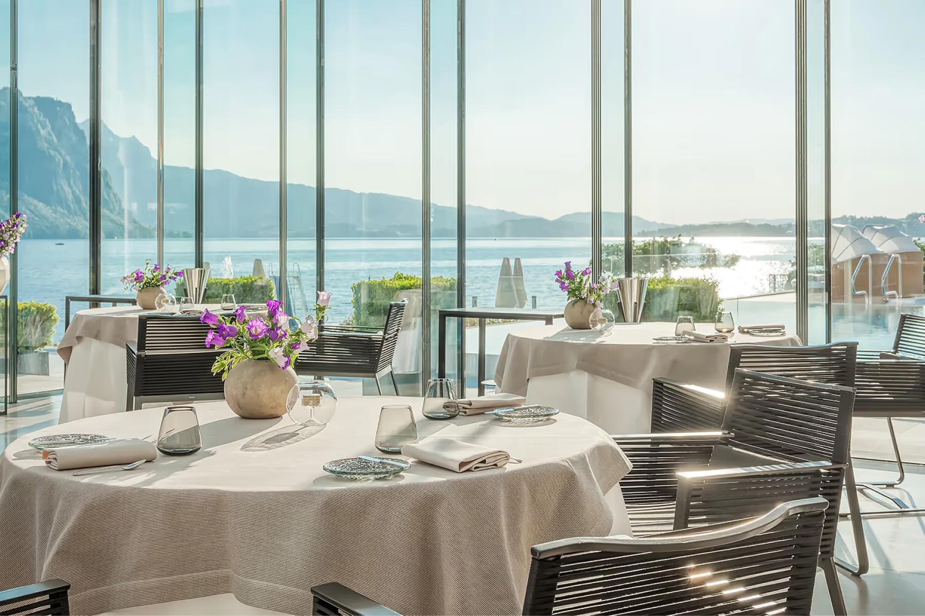 Dining room with round tables, floor-to-ceiling windows framing the lake
