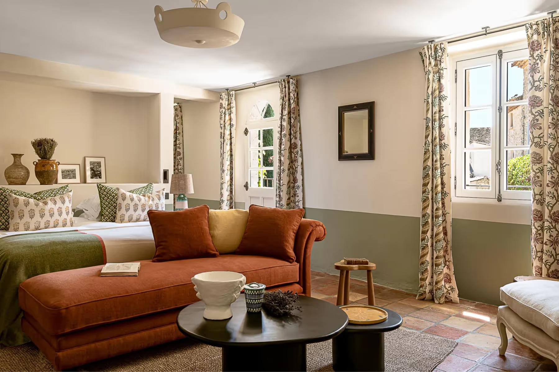 A sitting room with a rust-colored velvet sofa, mustard pillows, and green wall sections opposite a bed
