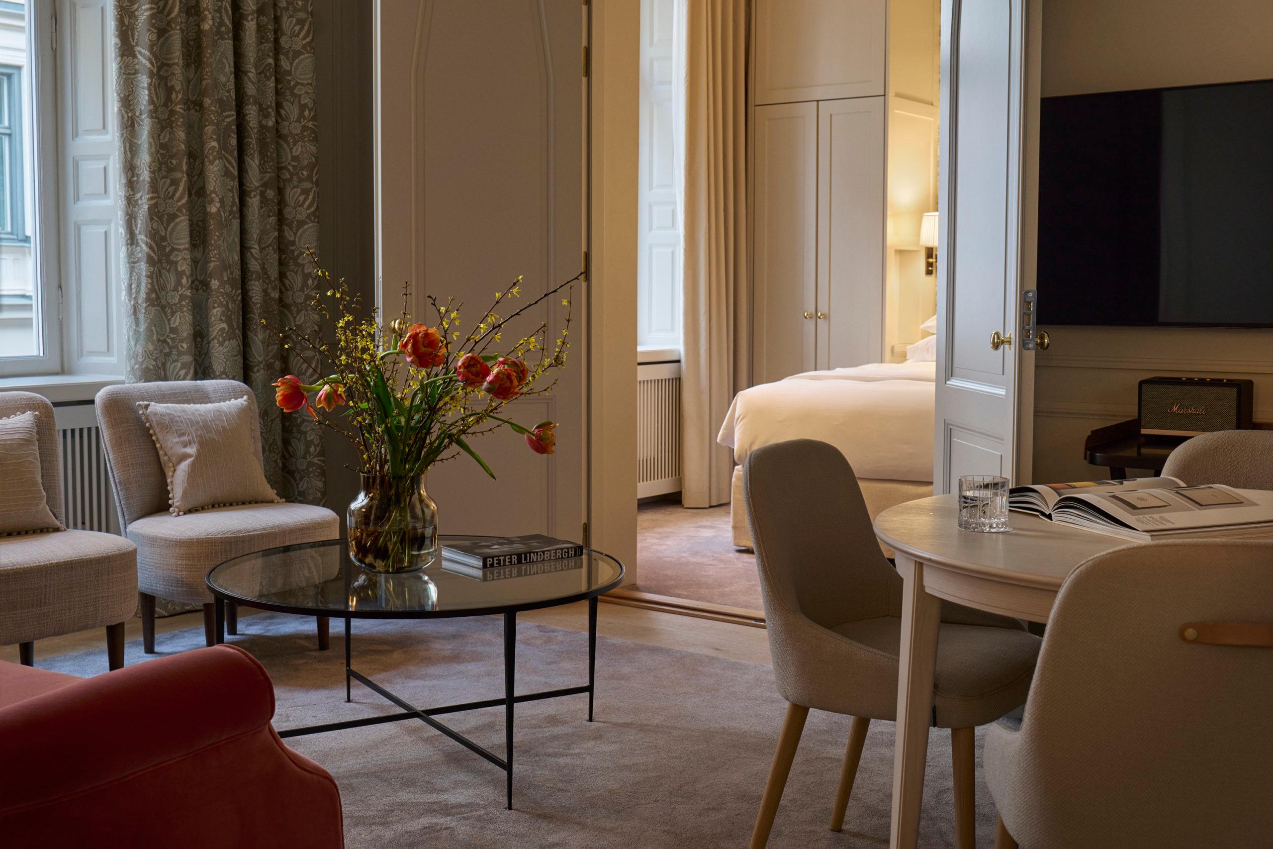 Villa Dagmar: suite living area with red accent seating, bedroom beyond, and arranged floral arrangement