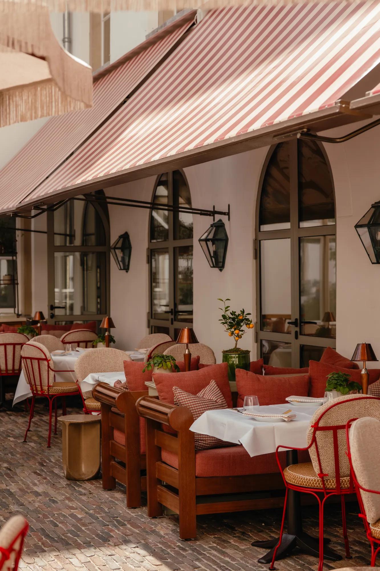 Rosewood Amsterdam: the Eeuwen terrace with a striped awning, lanterns, and red cushioned seats