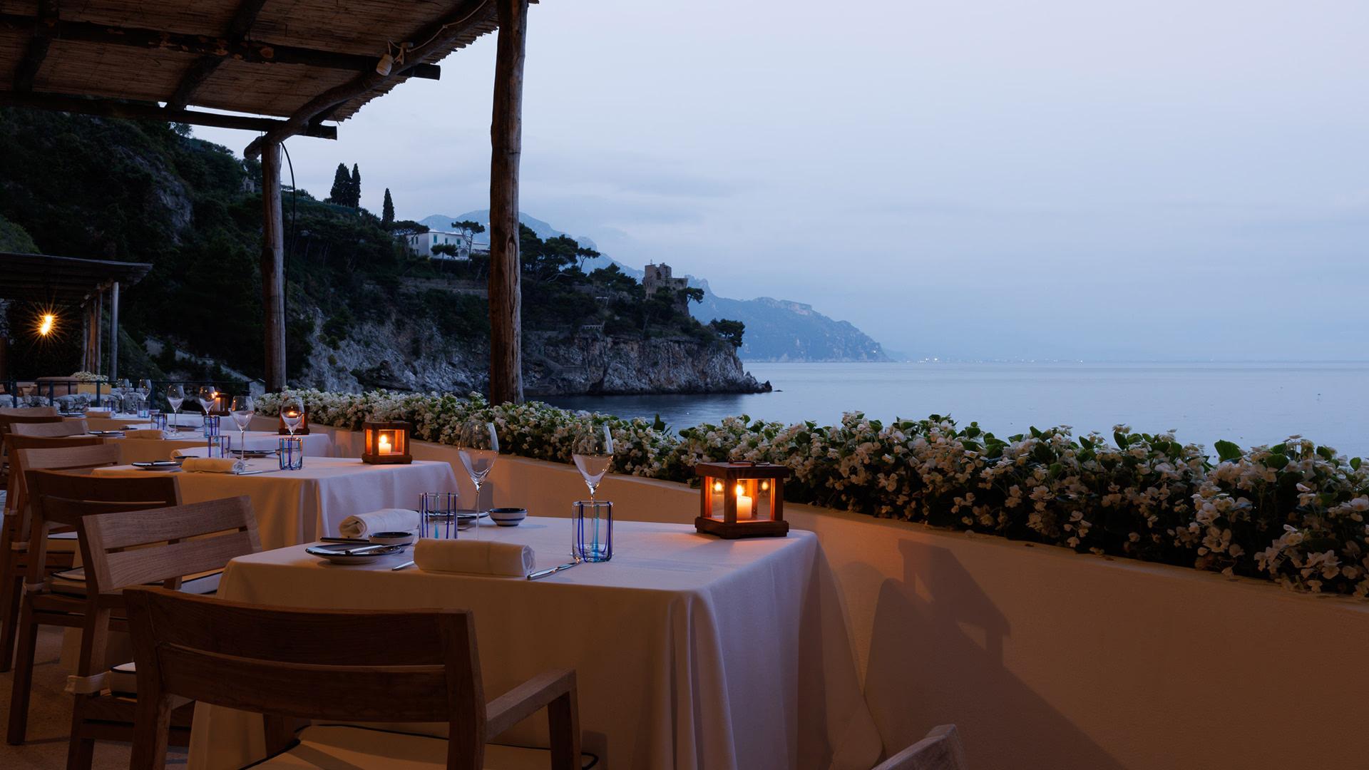 Candlelit dining setup on clifftop terrace at dusk with mountain horizon