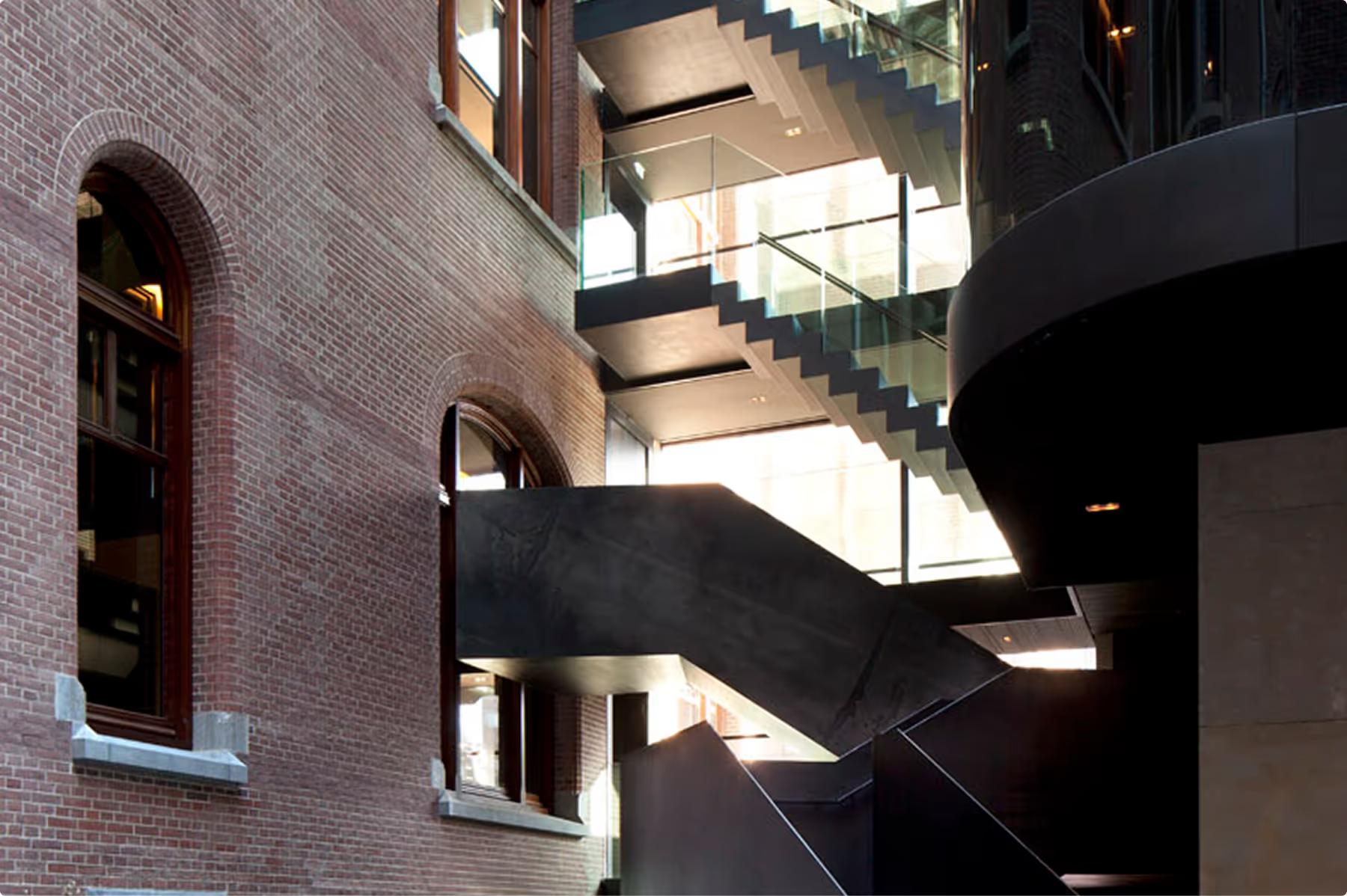 Mandarin Oriental Conservatorium, Amsterdam: angular black metal staircase crossing the atrium beside the arched windows of the brick building