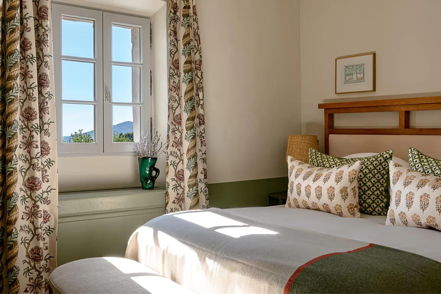 Hôtel Crillon le Brave: a bedroom with patterned green curtains, wooden shelving, twin beds with green blankets, and morning light