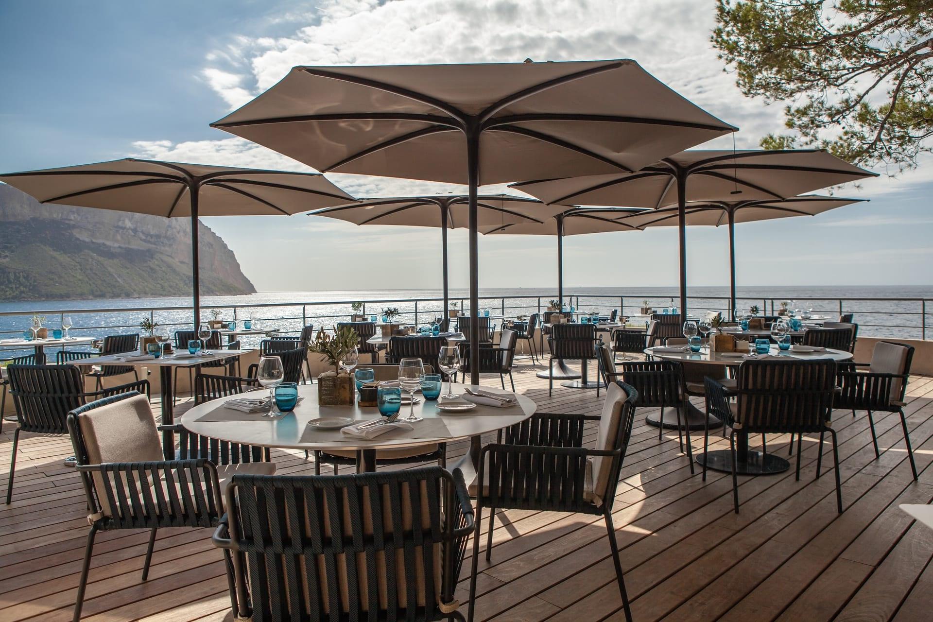 Les Roches Blanches: a seaside dining terrace with large umbrellas, wooden tables, and Mediterranean Sea beyond