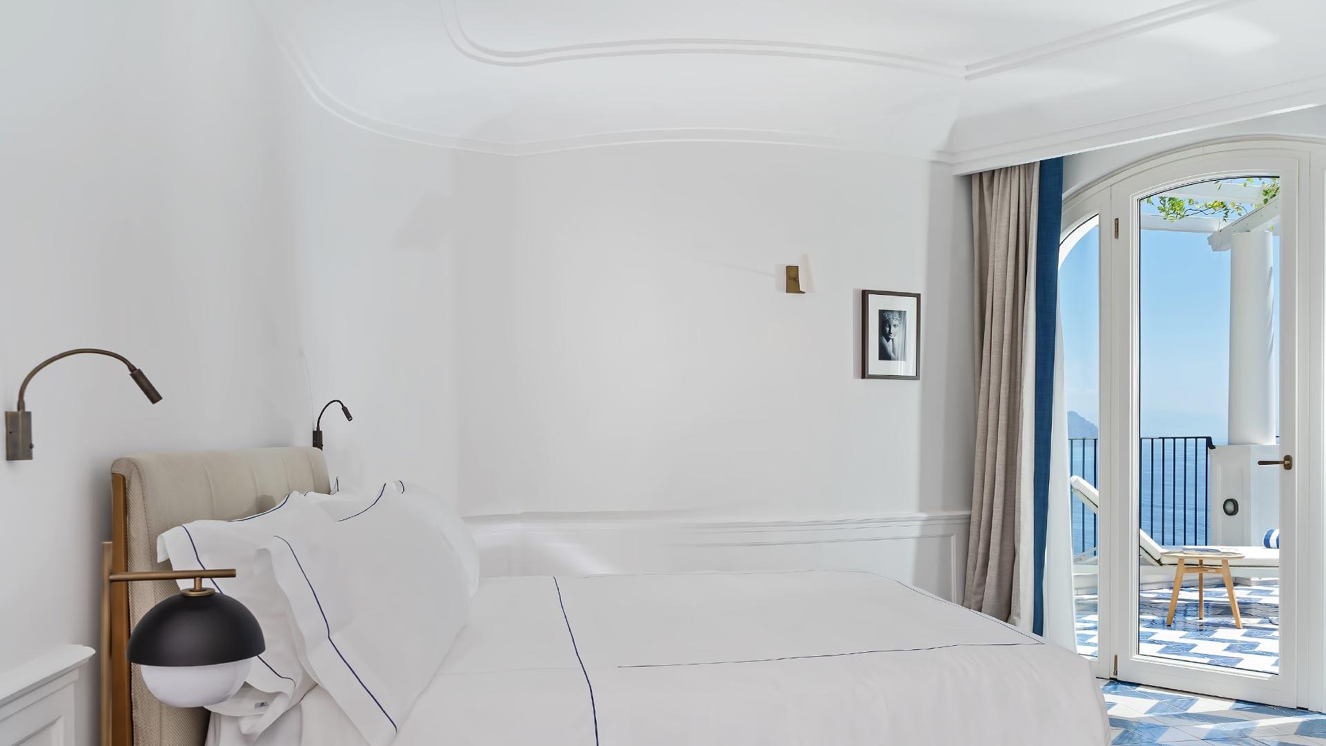 Minimalist bedroom with white bedding and ocean vista through glass doors at dusk