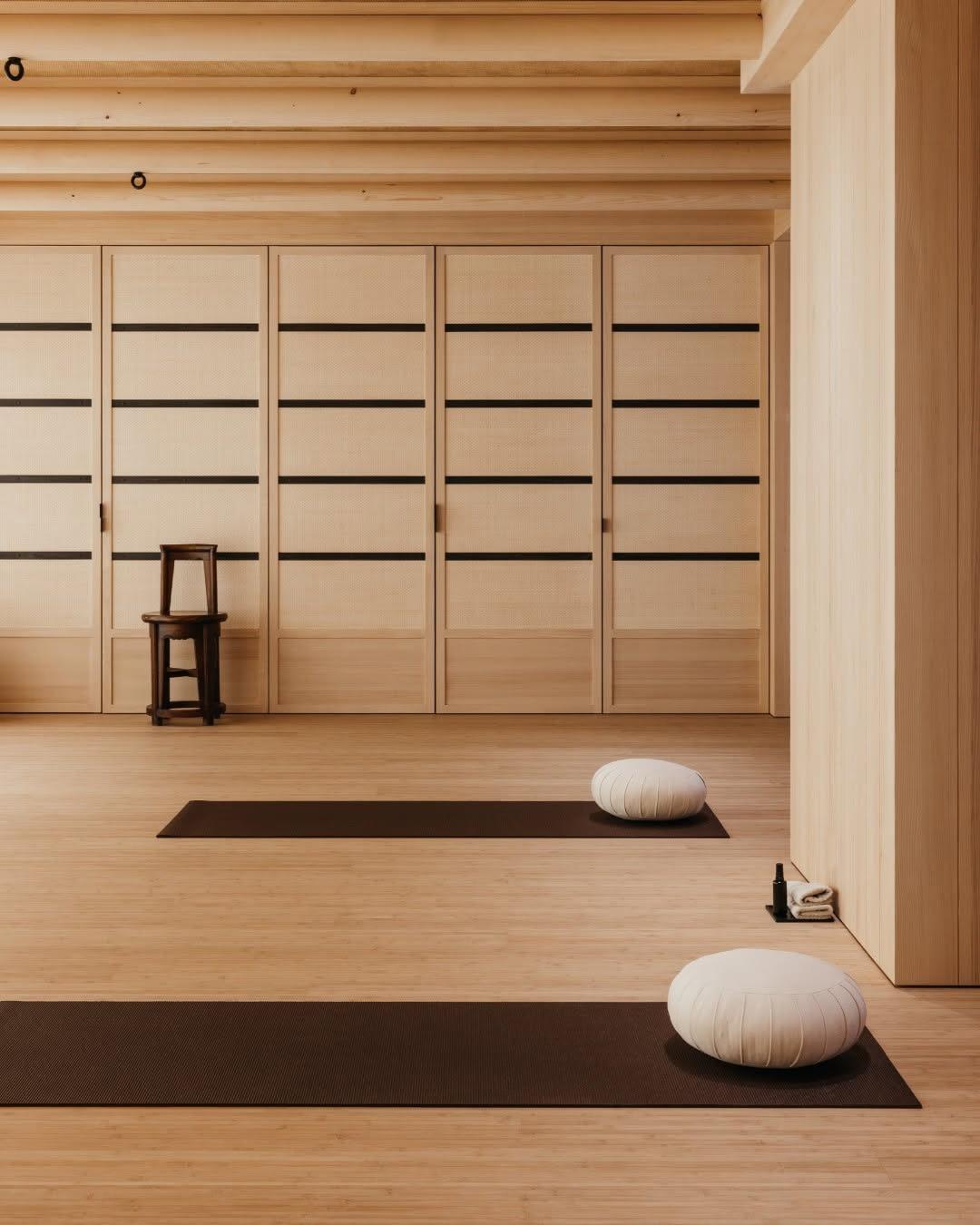 Yoga studio with two floor cushions on mats, a wooden stool, and an exposed beam ceiling