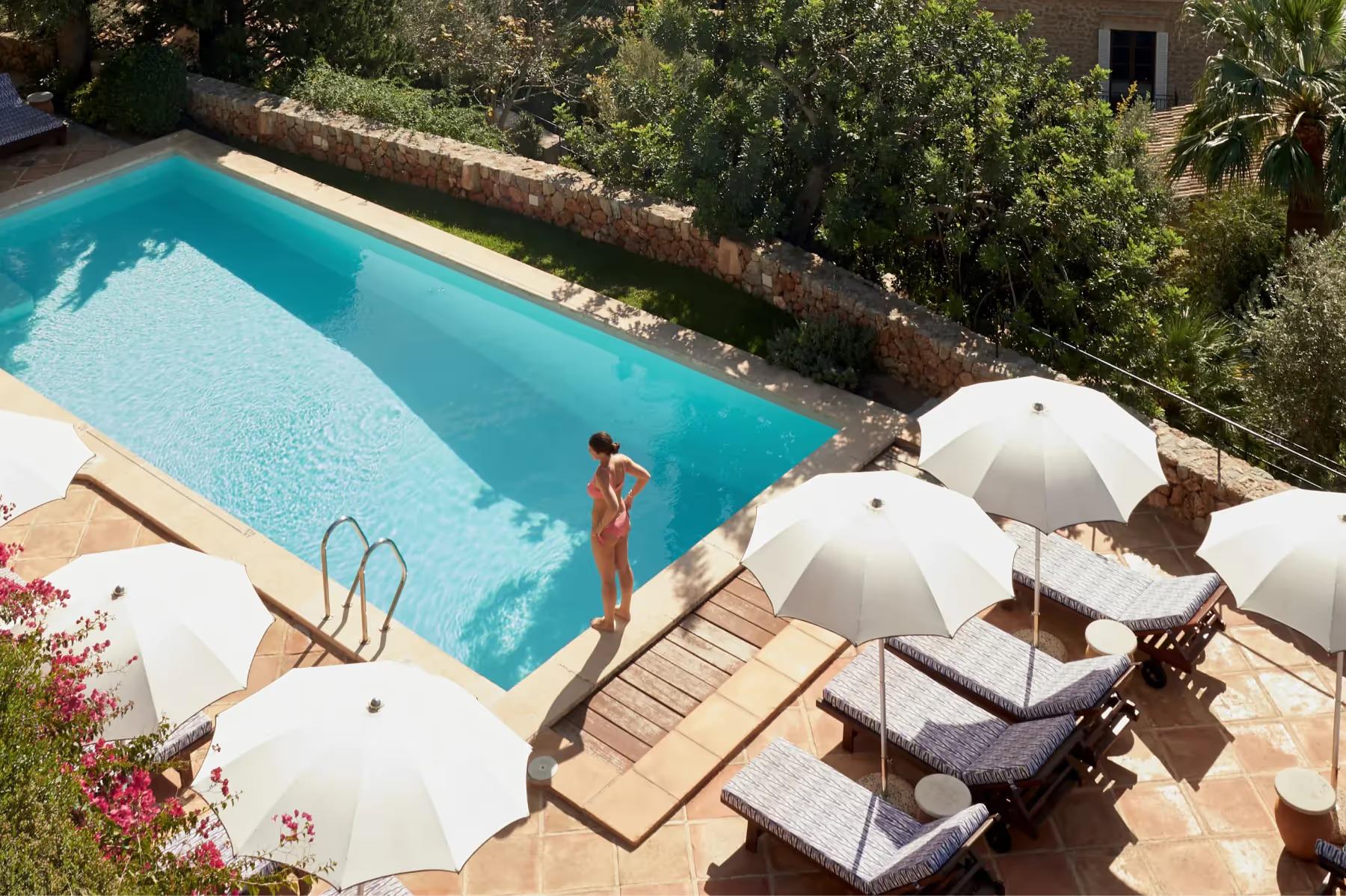 La Residencia: swimming pool with lounge chairs, white umbrellas, and stone building in background
