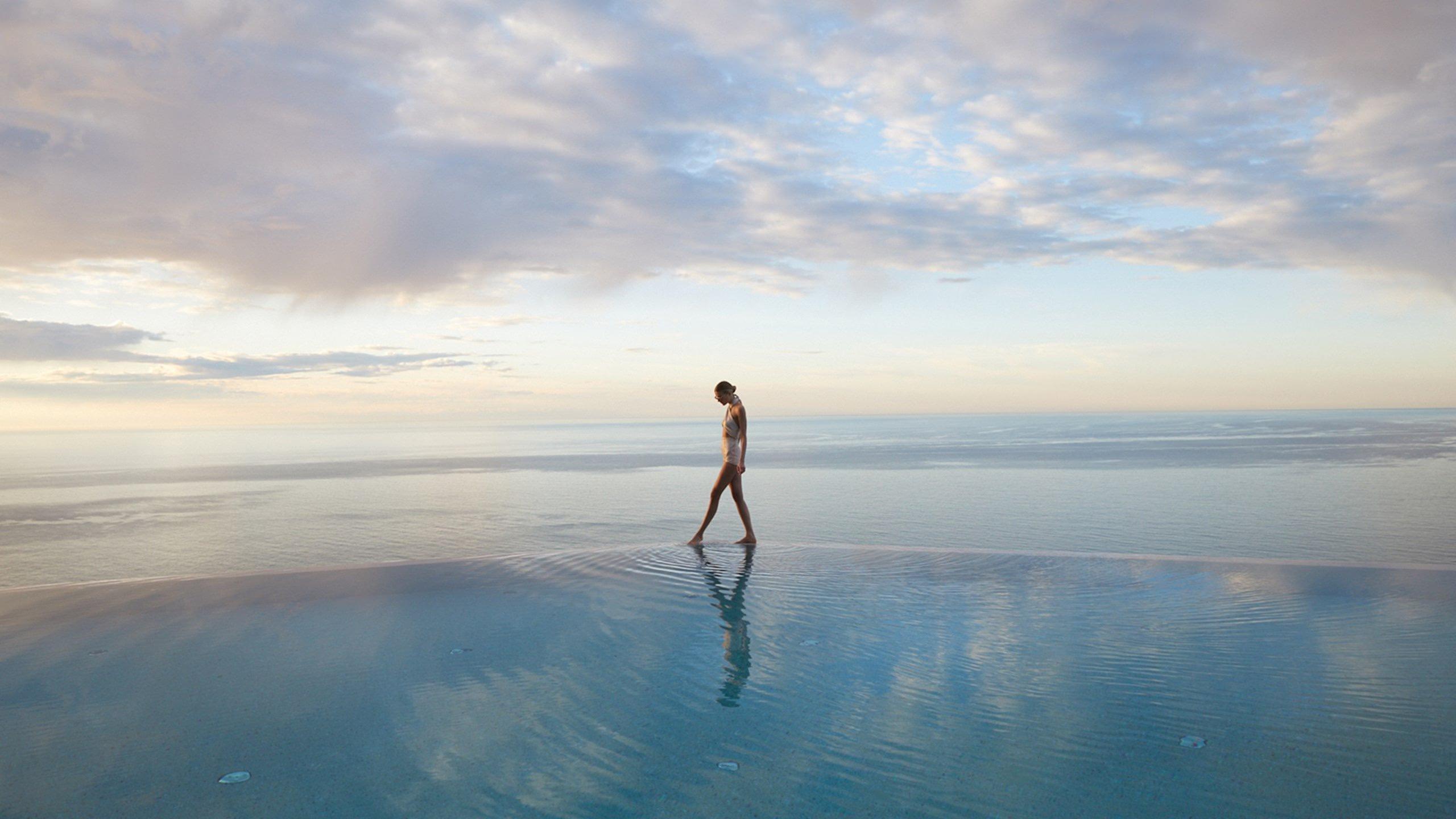 Figure at infinity pool mirroring sky and water