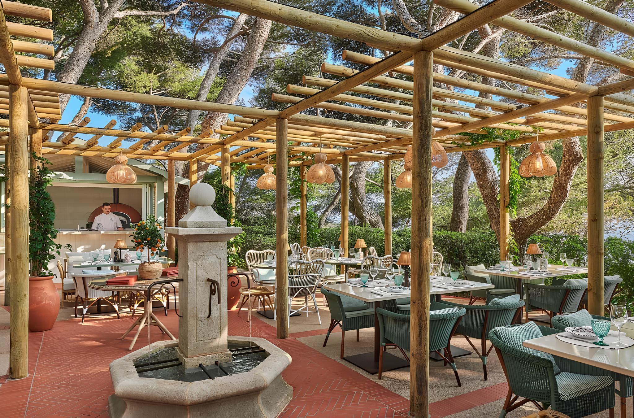 A covered outdoor restaurant with pergola structure, woven furnishings, and Mediterranean setting
