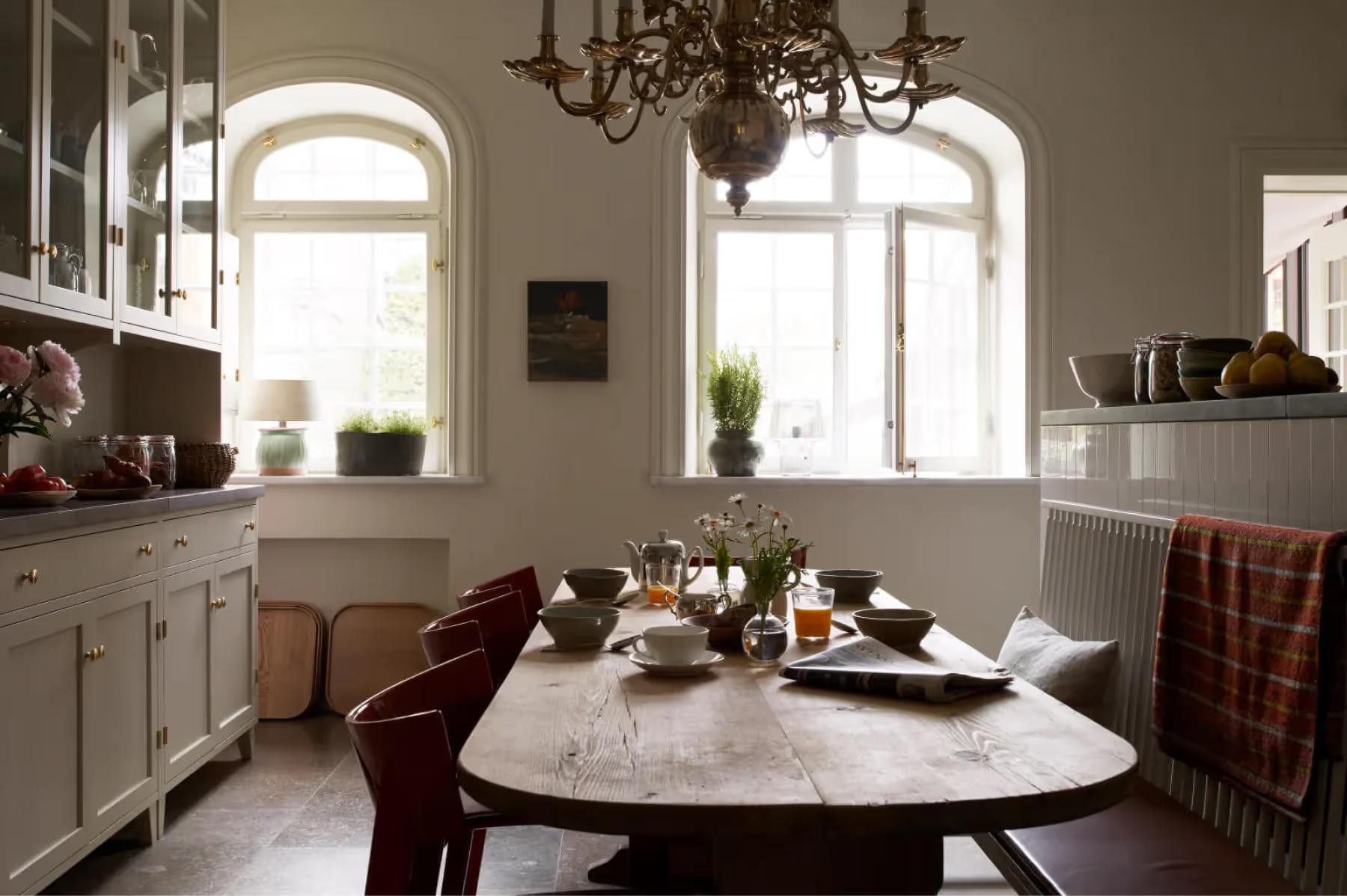 Ett Hem: a dining room with round marble table, arched windows, white chairs, and pendant lighting