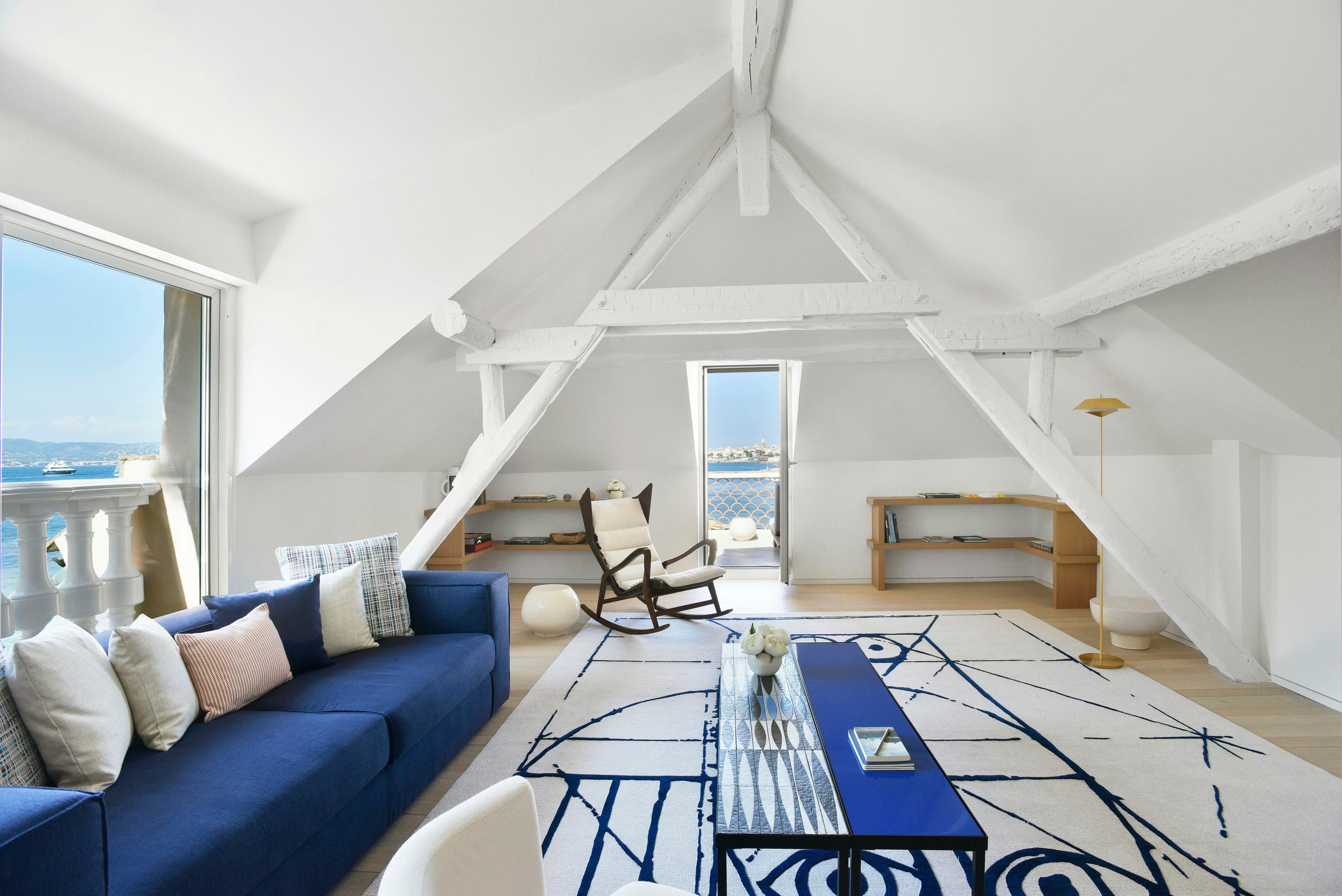 Vaulted white suite with blue sofa, patterned rug, and sea access