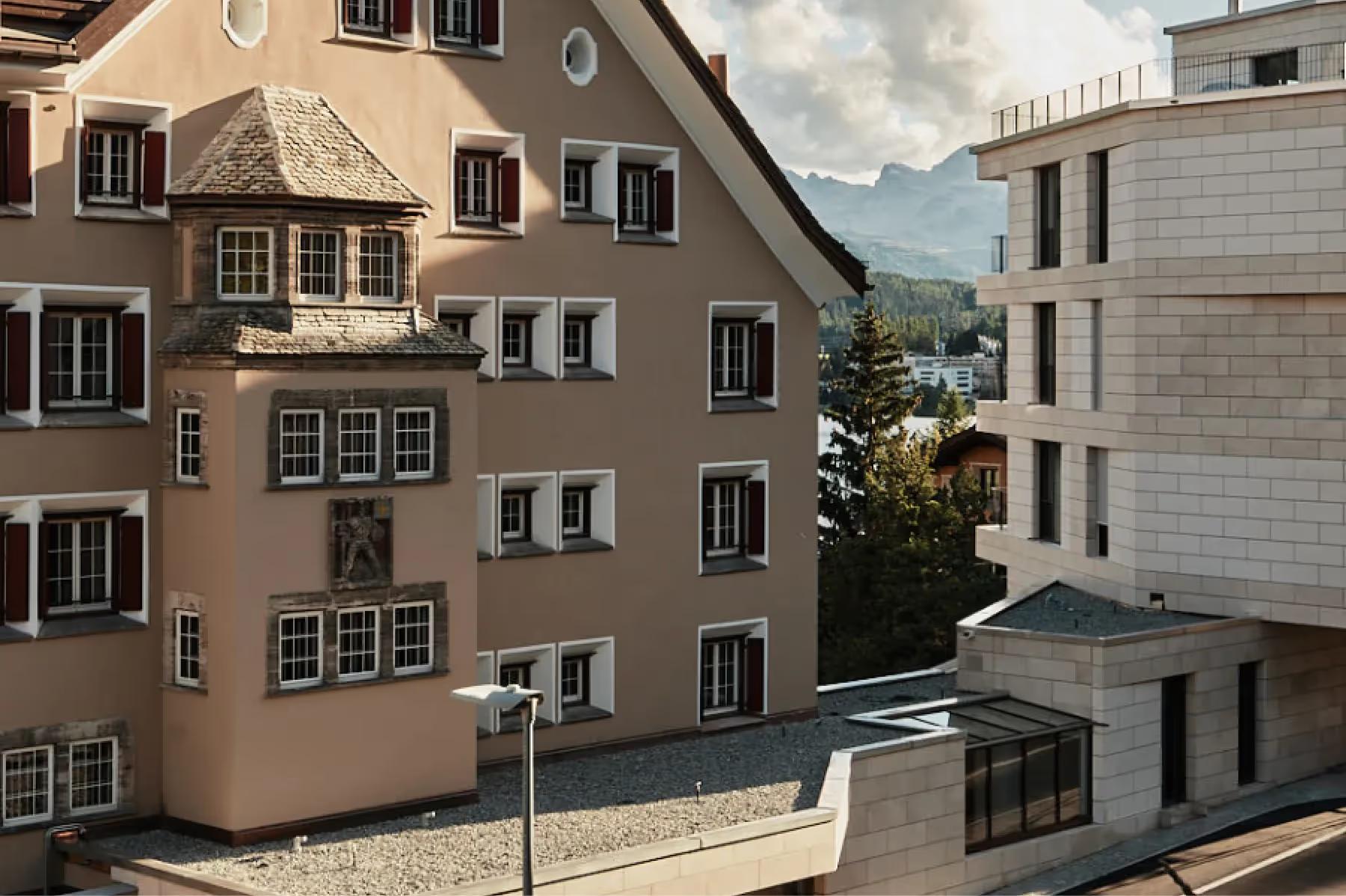Historic stone buildings with mountains in the distance and alpine meadow below