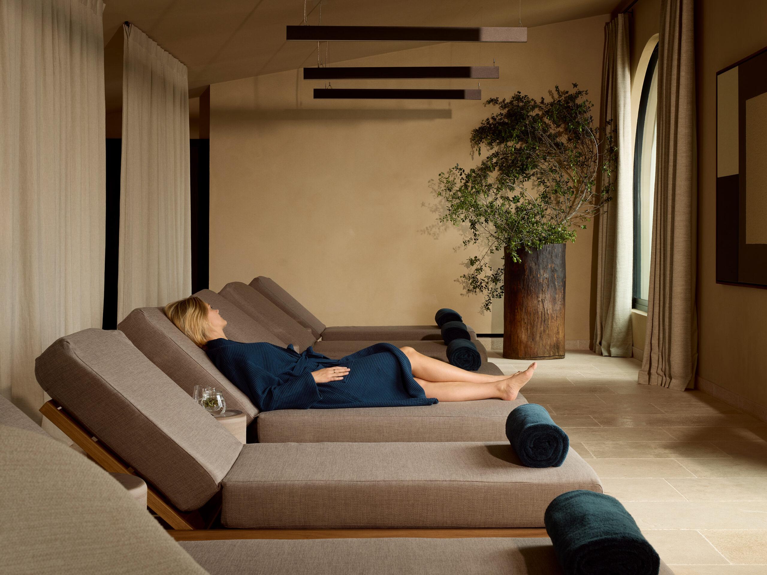 Zannier Île de Bendor: a guest in a robe reclines on a spa lounger beneath pendant lights and a potted olive tree
