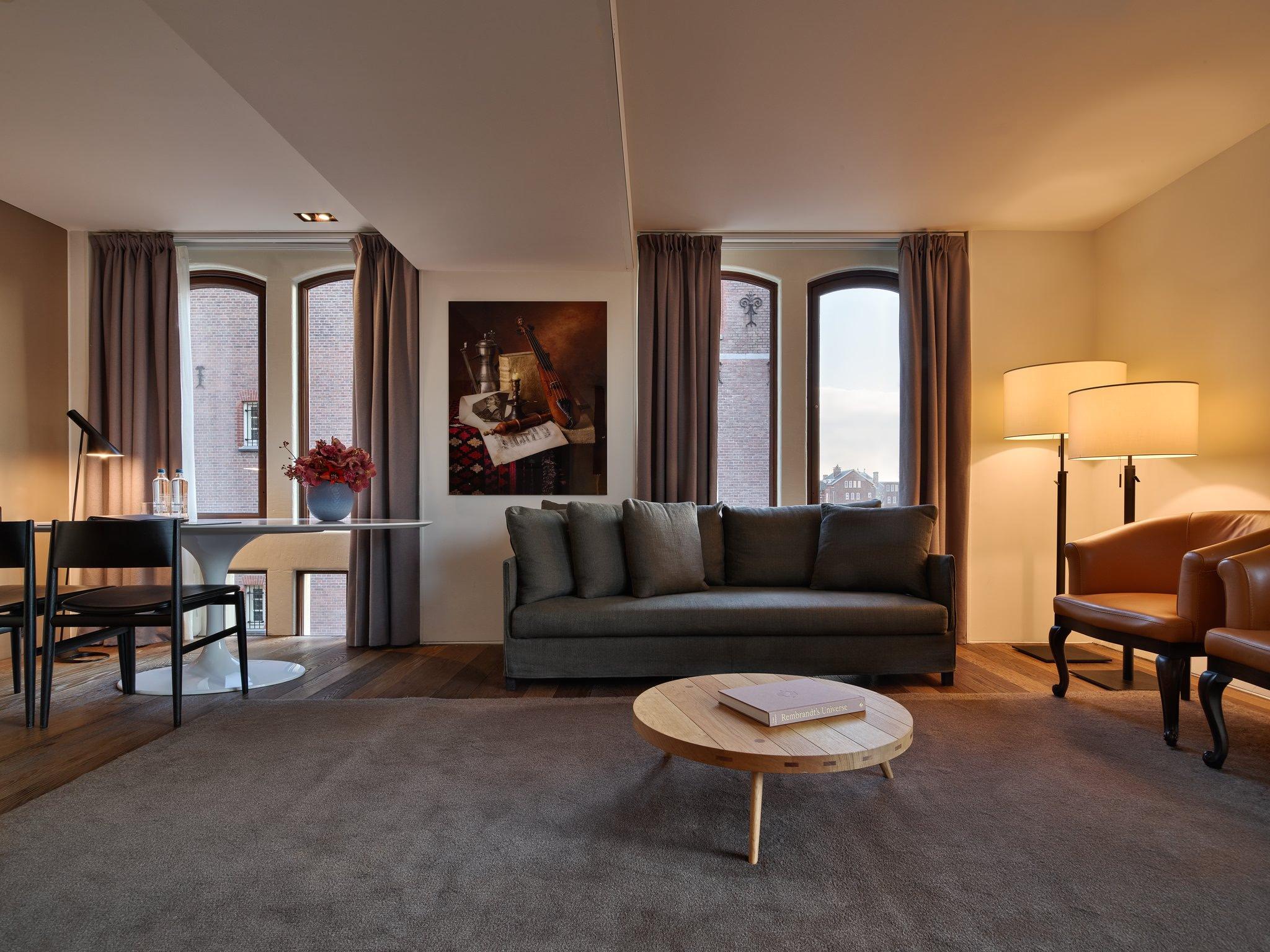 Mandarin Oriental Conservatorium, Amsterdam: living room with a grey sofa, a wooden coffee table, two armchairs, and arched windows