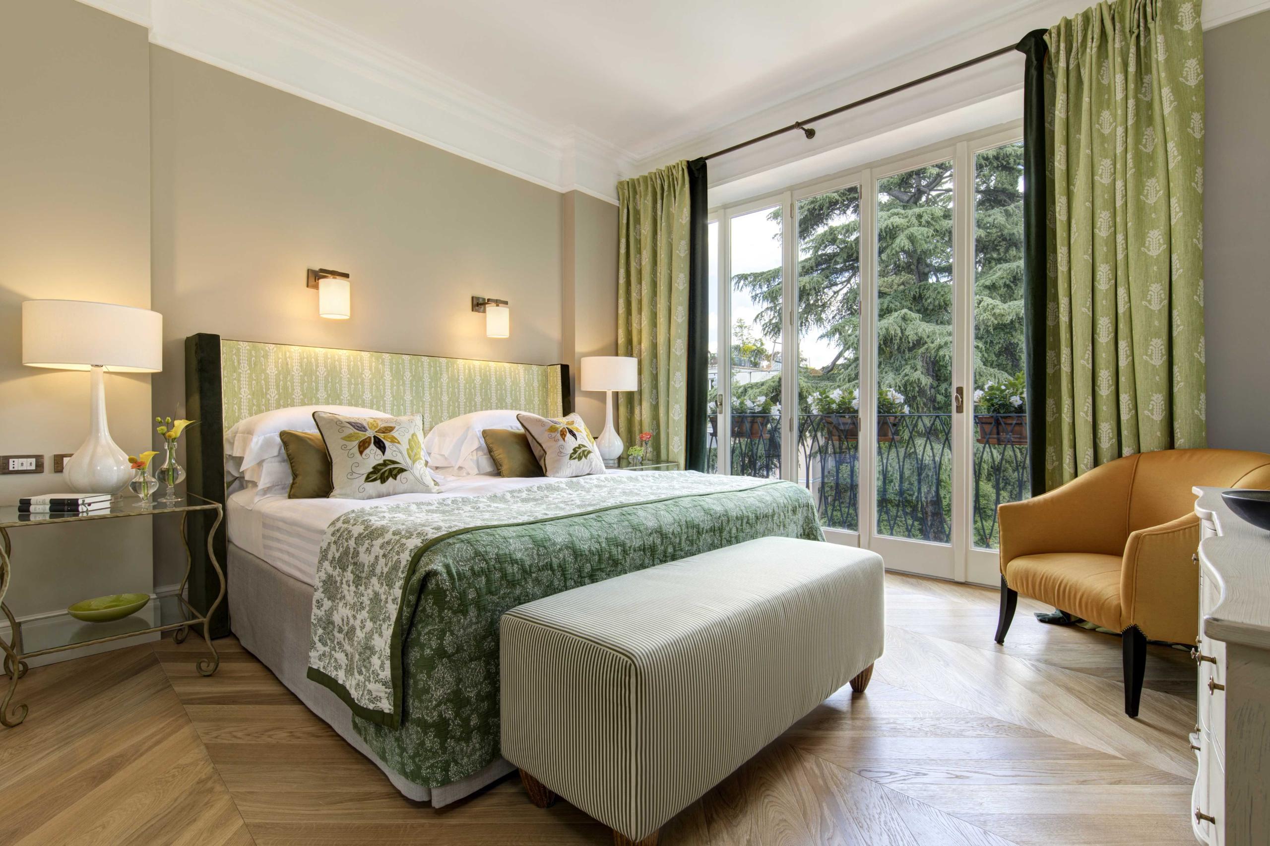 Bedroom with green patterned bedspread, marble accents, and large windows with garden views