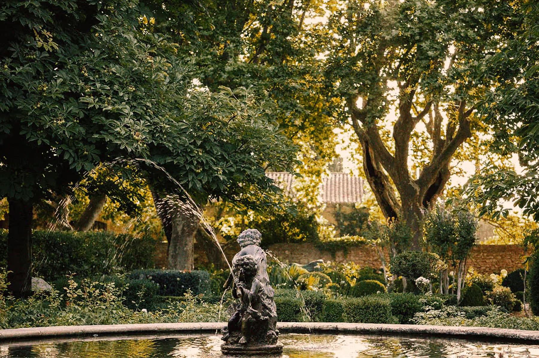 Fountain sculpture in garden courtyard surrounded by stone walls and mature trees