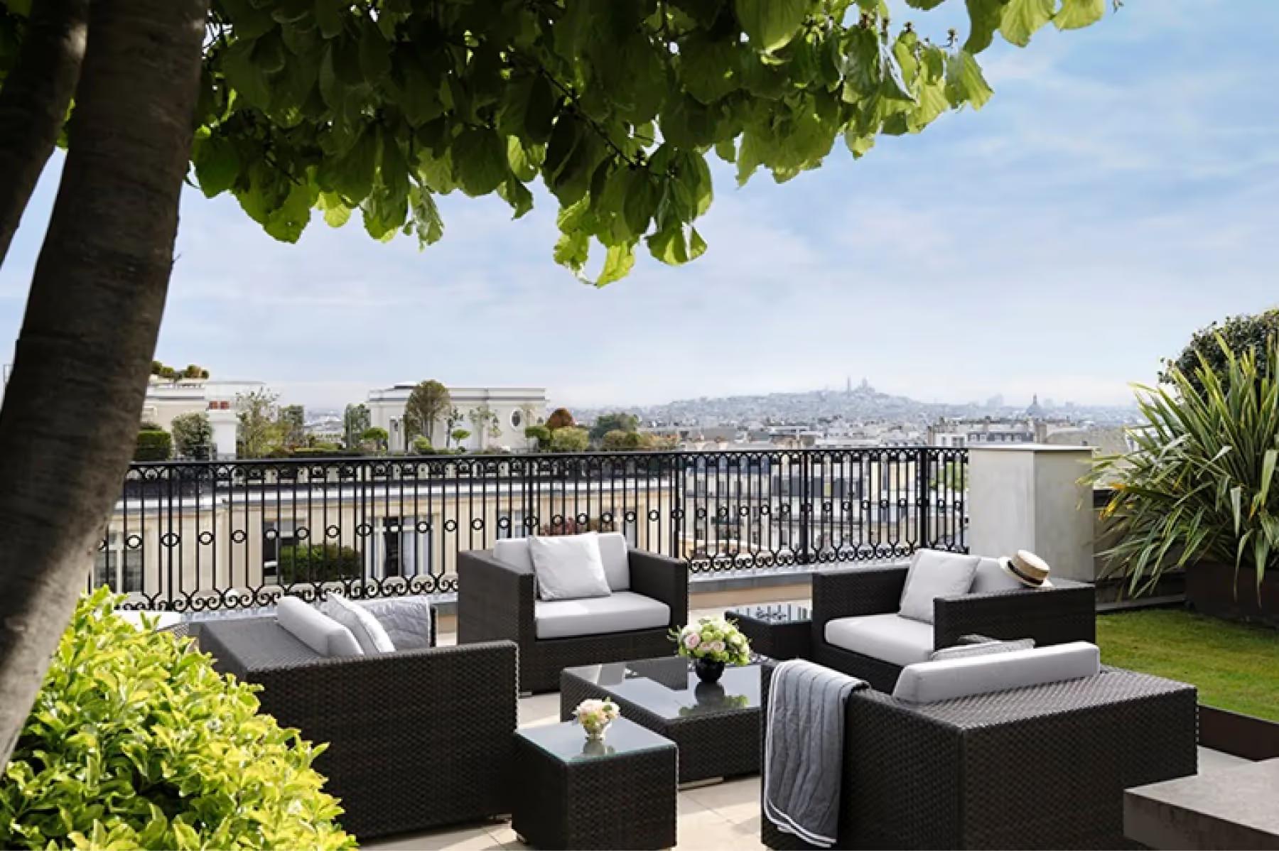 Rooftop terrace with shade trees, black lounge furniture, Paris cityscape, and overcast sky