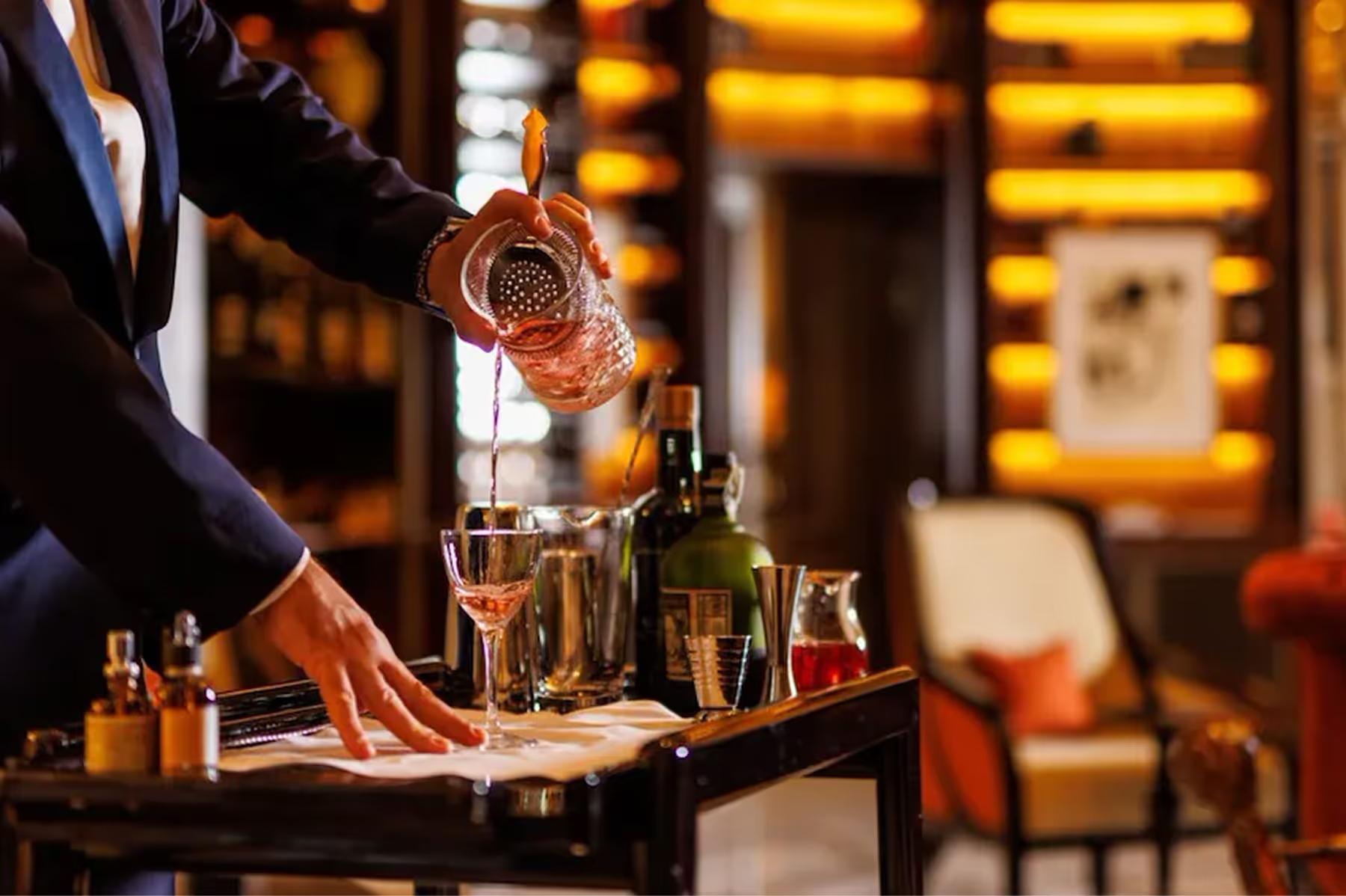 Hotel Eden: a hand pouring amber spirit into a glass at a marble bar counter with bottles in the background