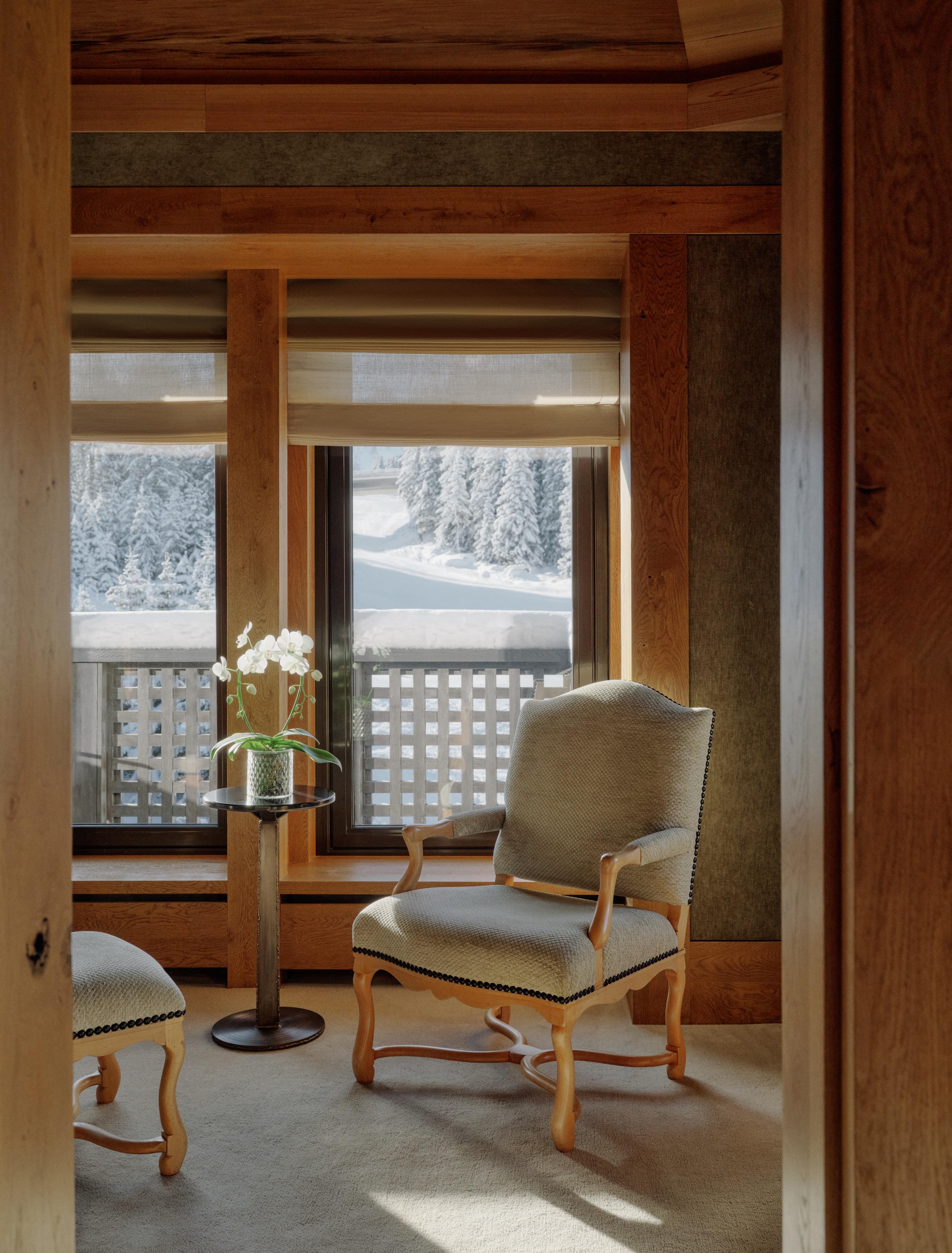 Aman Le Mélézin: reading nook with an upholstered armchair, ottoman, and orchid table beside a snowy window