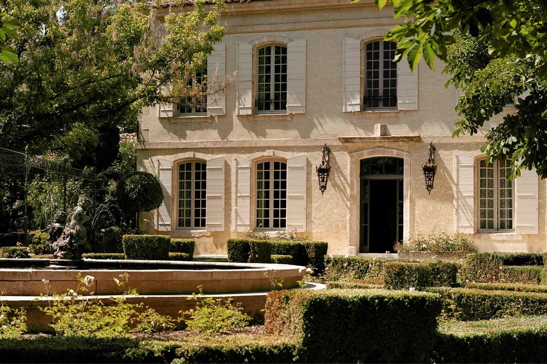 Le Mas de Chabran: pale stone facade with arched entry, dark shutters, and manicured hedge border
