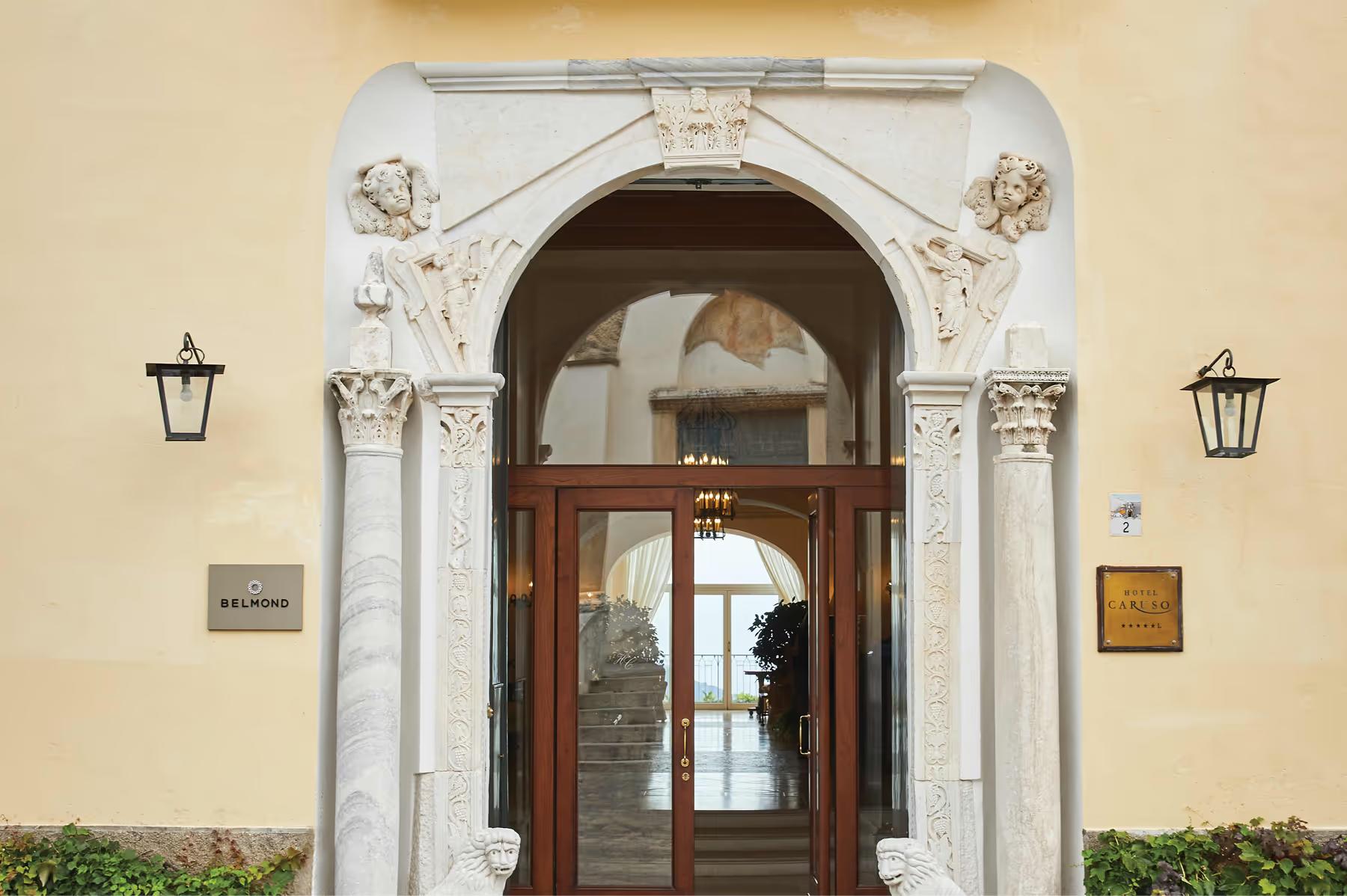 Ornate arched entry with carved columns, dark wood doors, and brass fixtures on cream facade