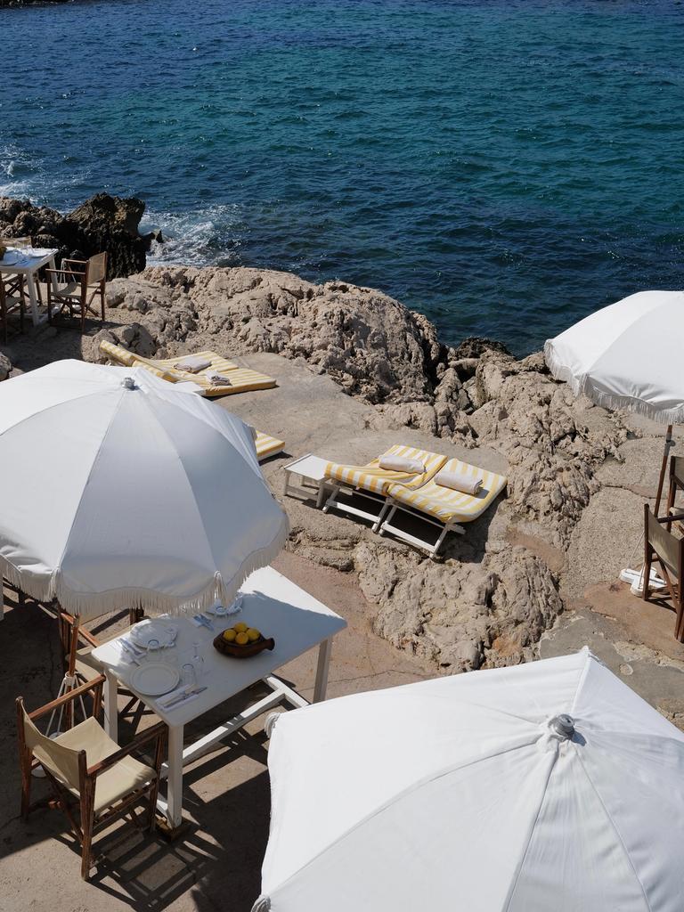 Striped loungers, white parasols and a set table on the rocks at Tuba Club, the sea beyond