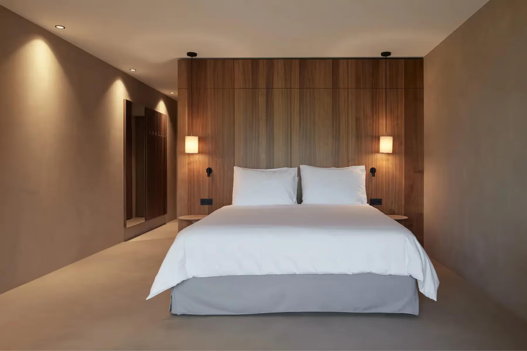 Hotel Saltus: modern bedroom with white bed and warm wood headboard wall under soft recessed lighting