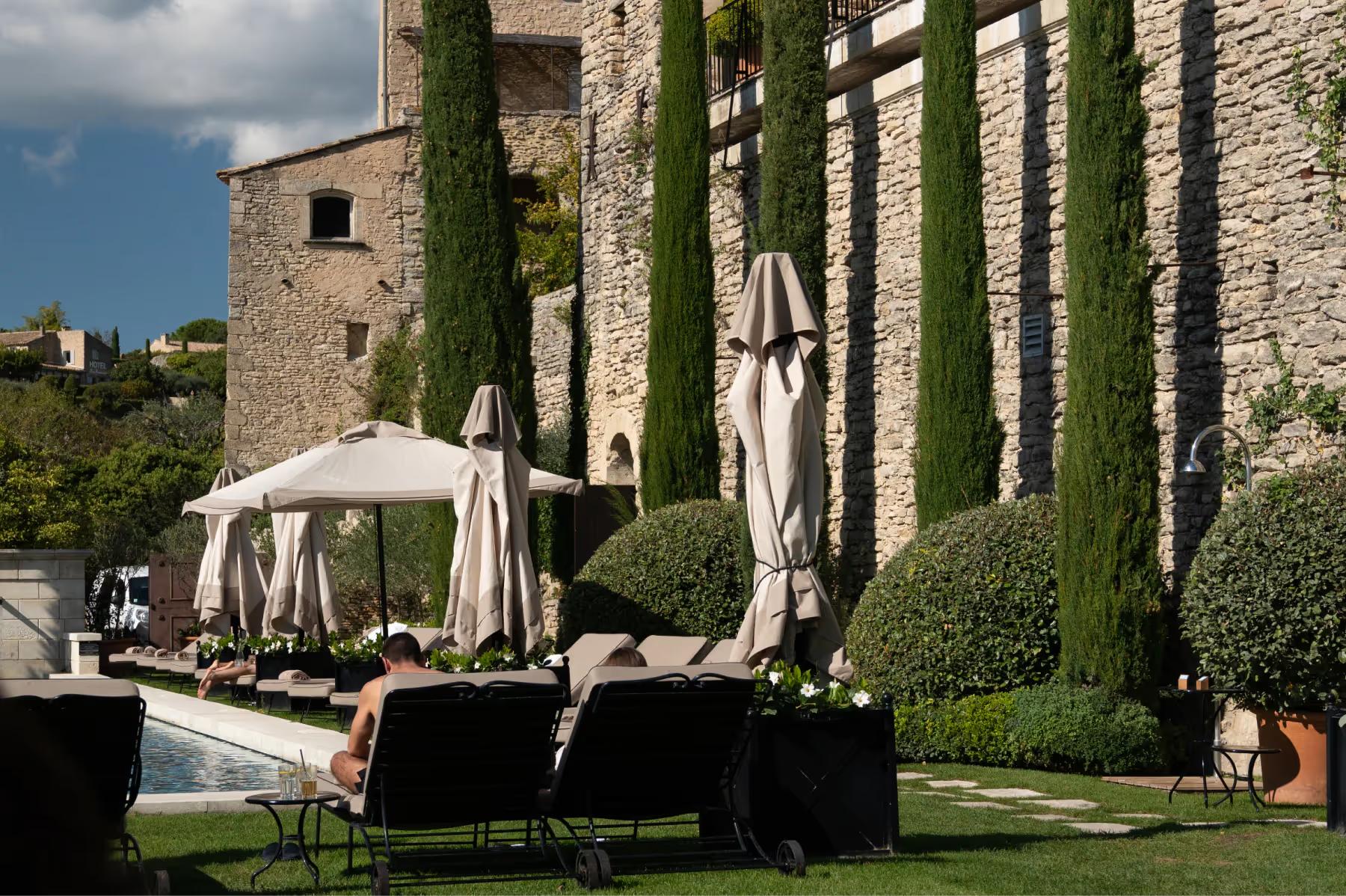 Airelles Gordes, La Bastide: poolside lounge area with stone walls and ivy-covered pergola