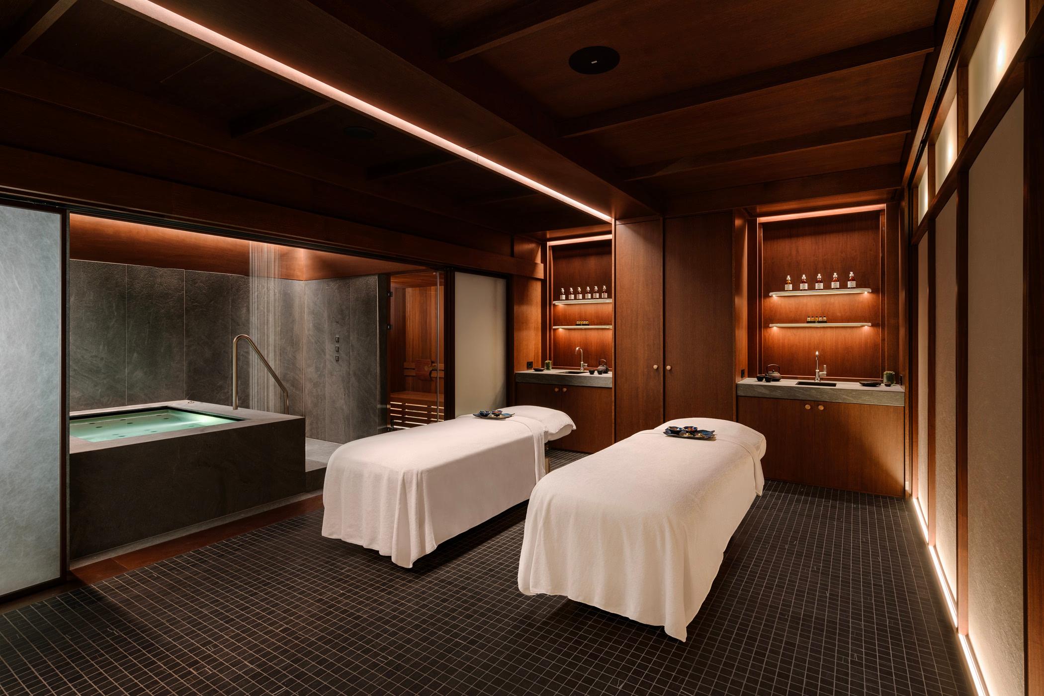 Spa treatment area with two massage beds, warm wood tones, and soft ambient lighting