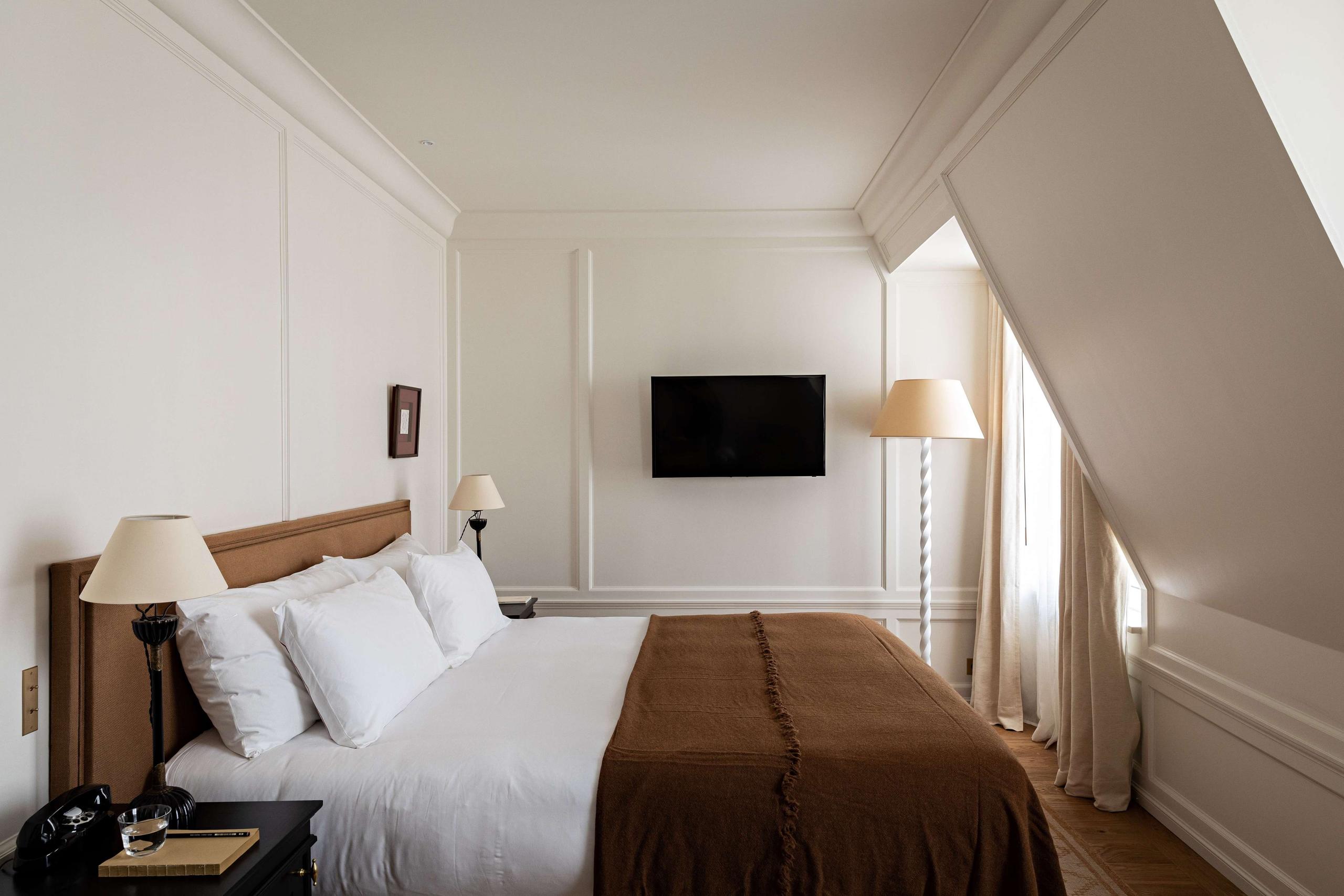 A bright bedroom with a wood platform bed, white pillows, and sloped ceiling