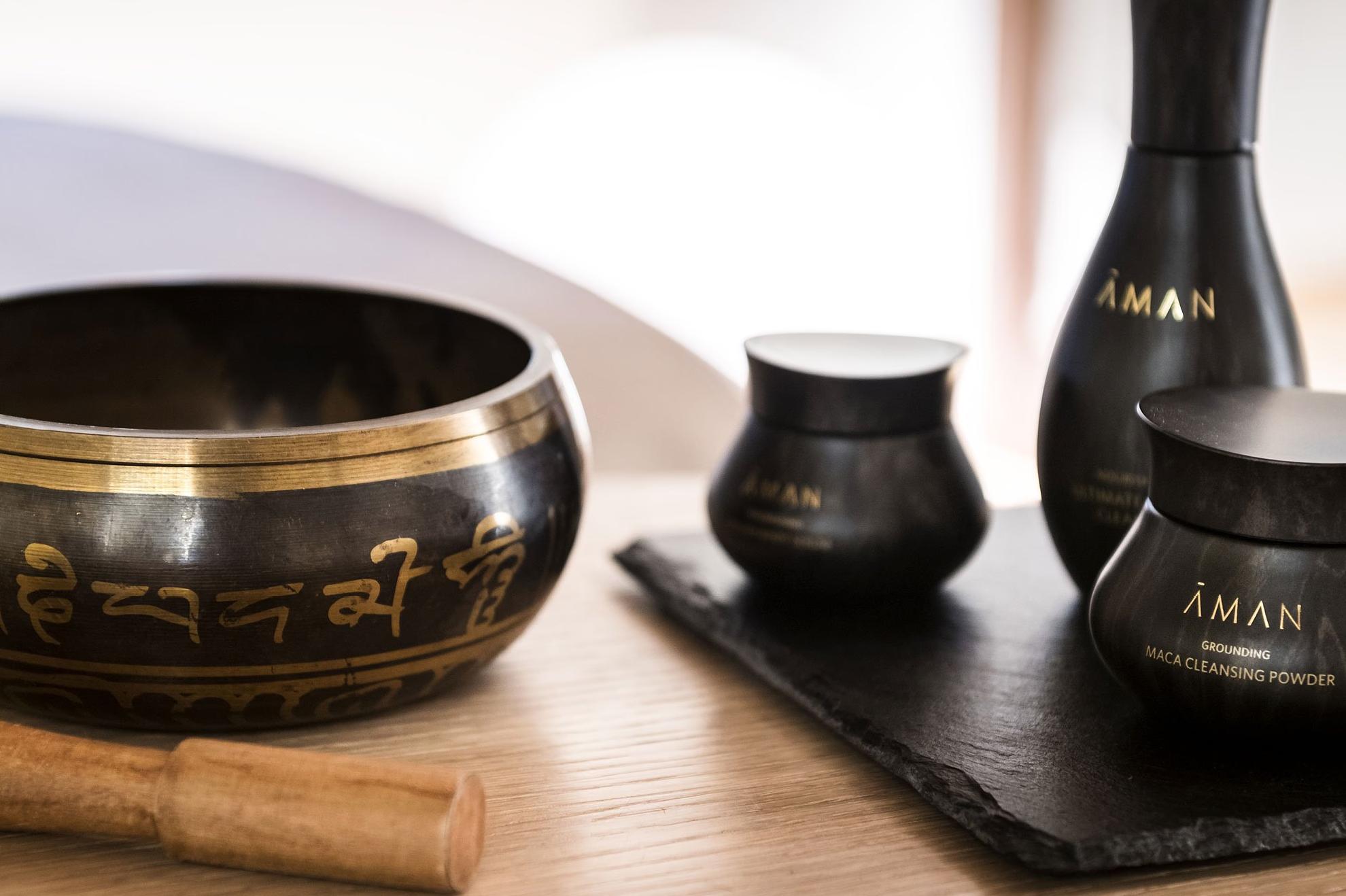 Aman wellness products including a black singing bowl, wooden mallet, and branded bottles