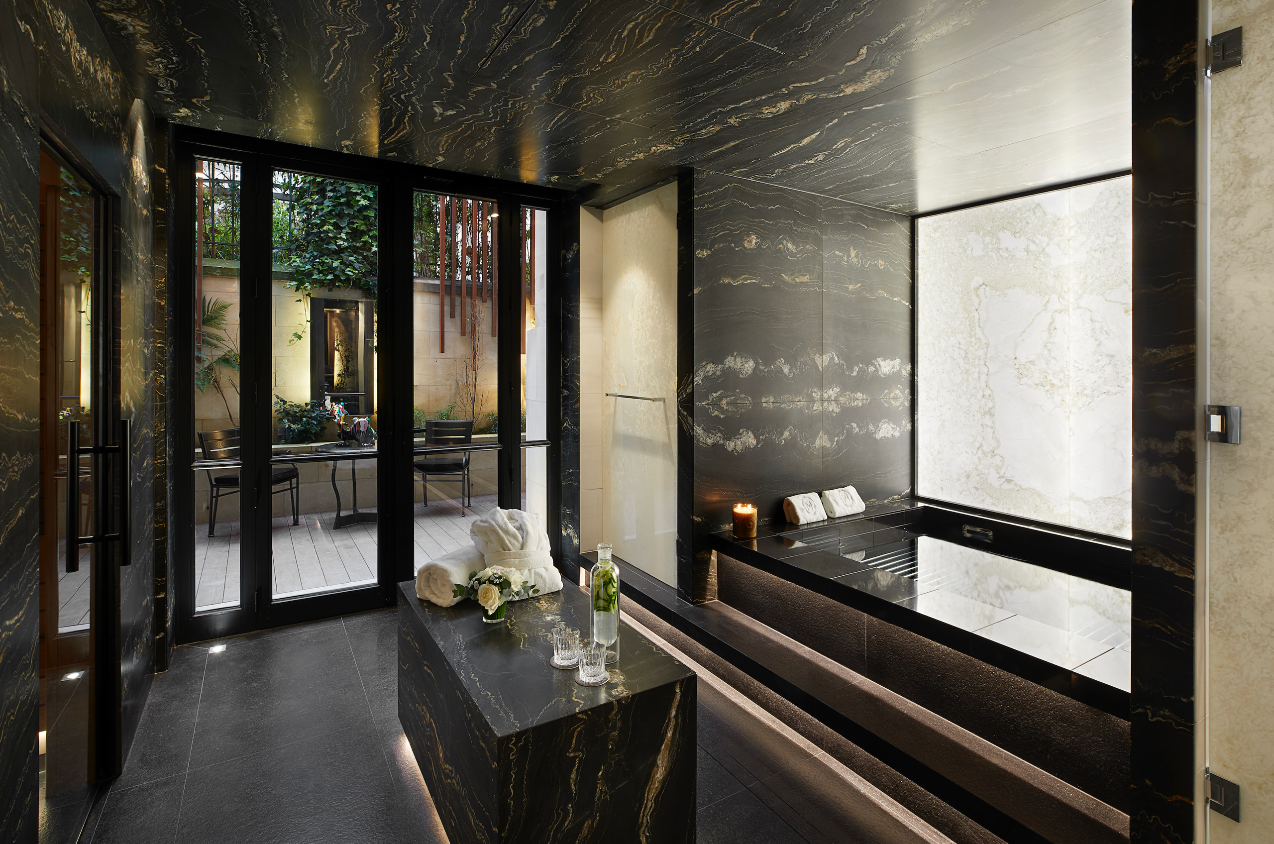 A spa interior with glass doors, dark marble walls, light fixtures, and contemporary furnishings