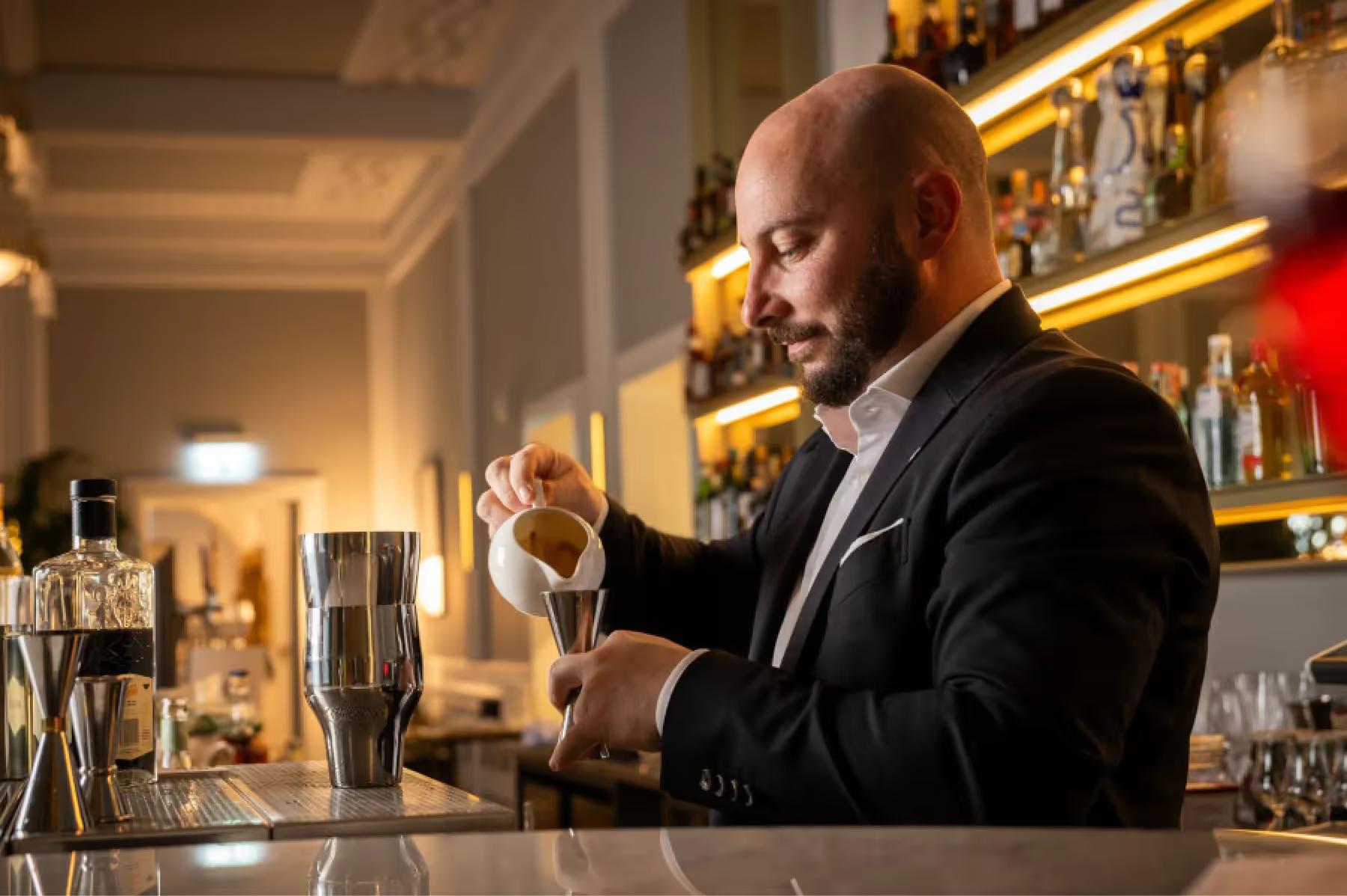 Bartender in suit pouring a drink at an illuminated bar counter