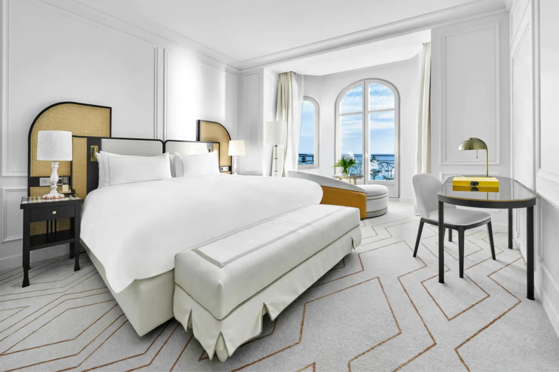 Bedroom with white linens, brass-trimmed nightstands, and glass doors leading to a sea-view balcony