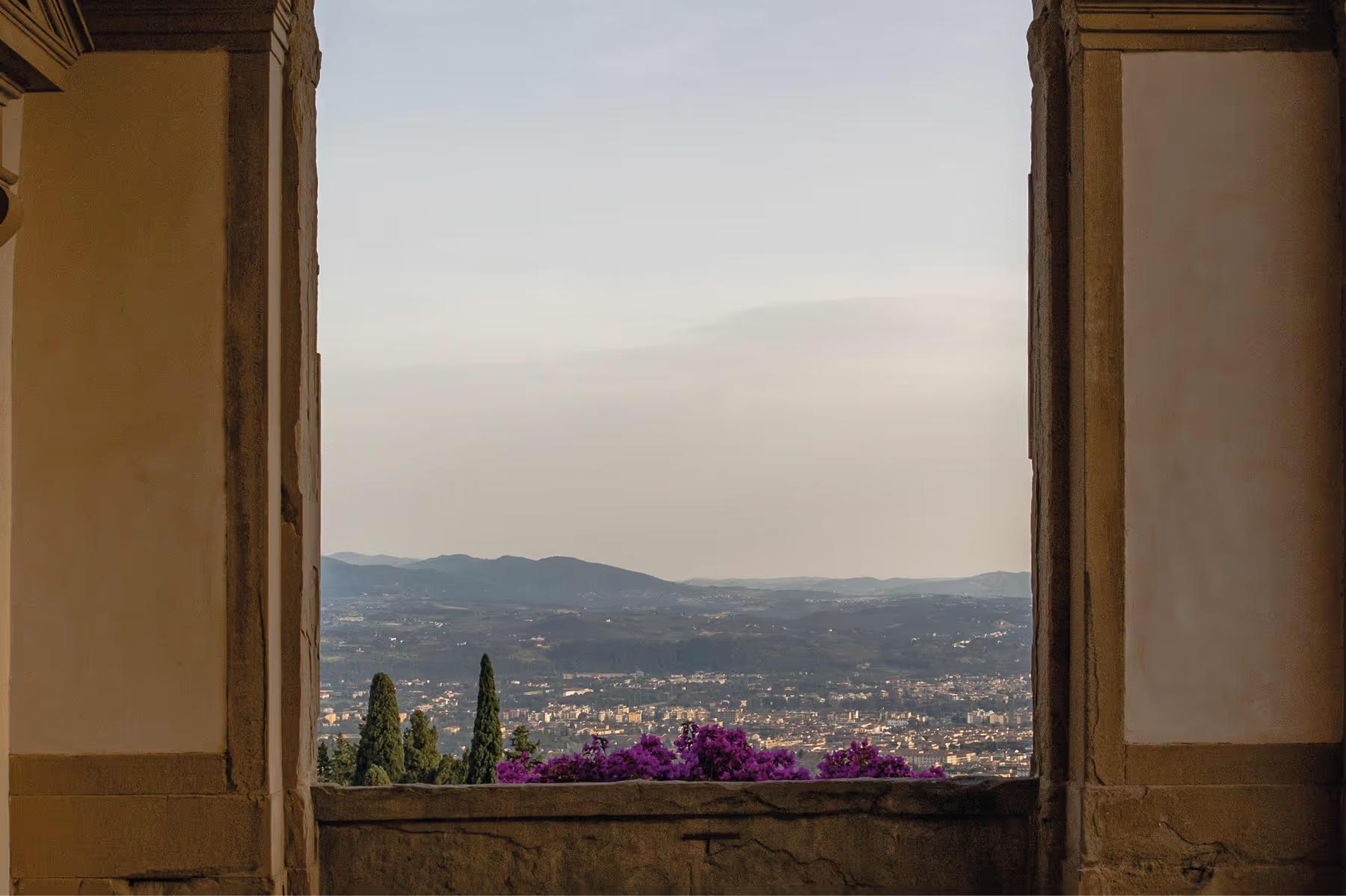 Villa San Michele: stone window opening with magenta flowers, cypress trees, and sweeping view across the Tuscan countryside