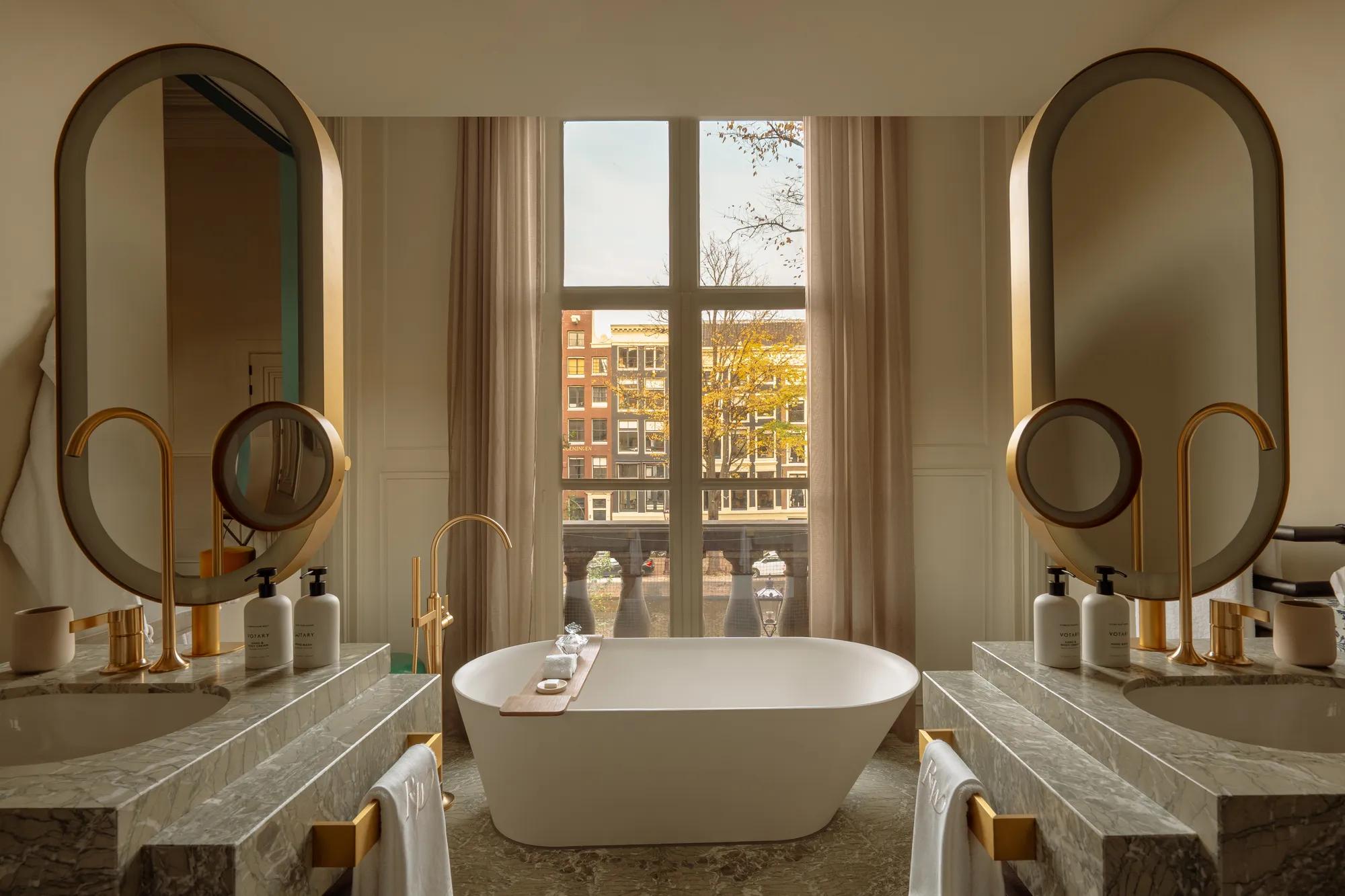 Rosewood Amsterdam: a Canal View Signature Suite bathroom with a freestanding tub between two marble vanities