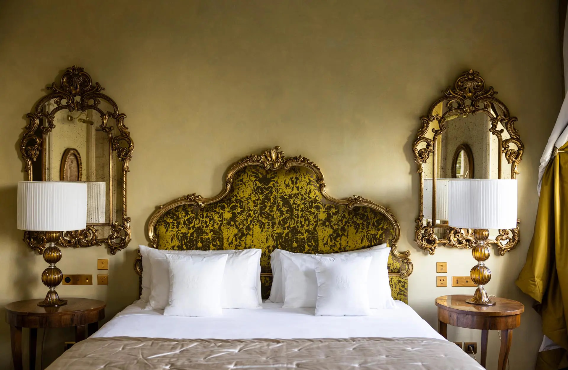 A bed with ornate gold headboard flanked by mirrored bedside tables and sconces