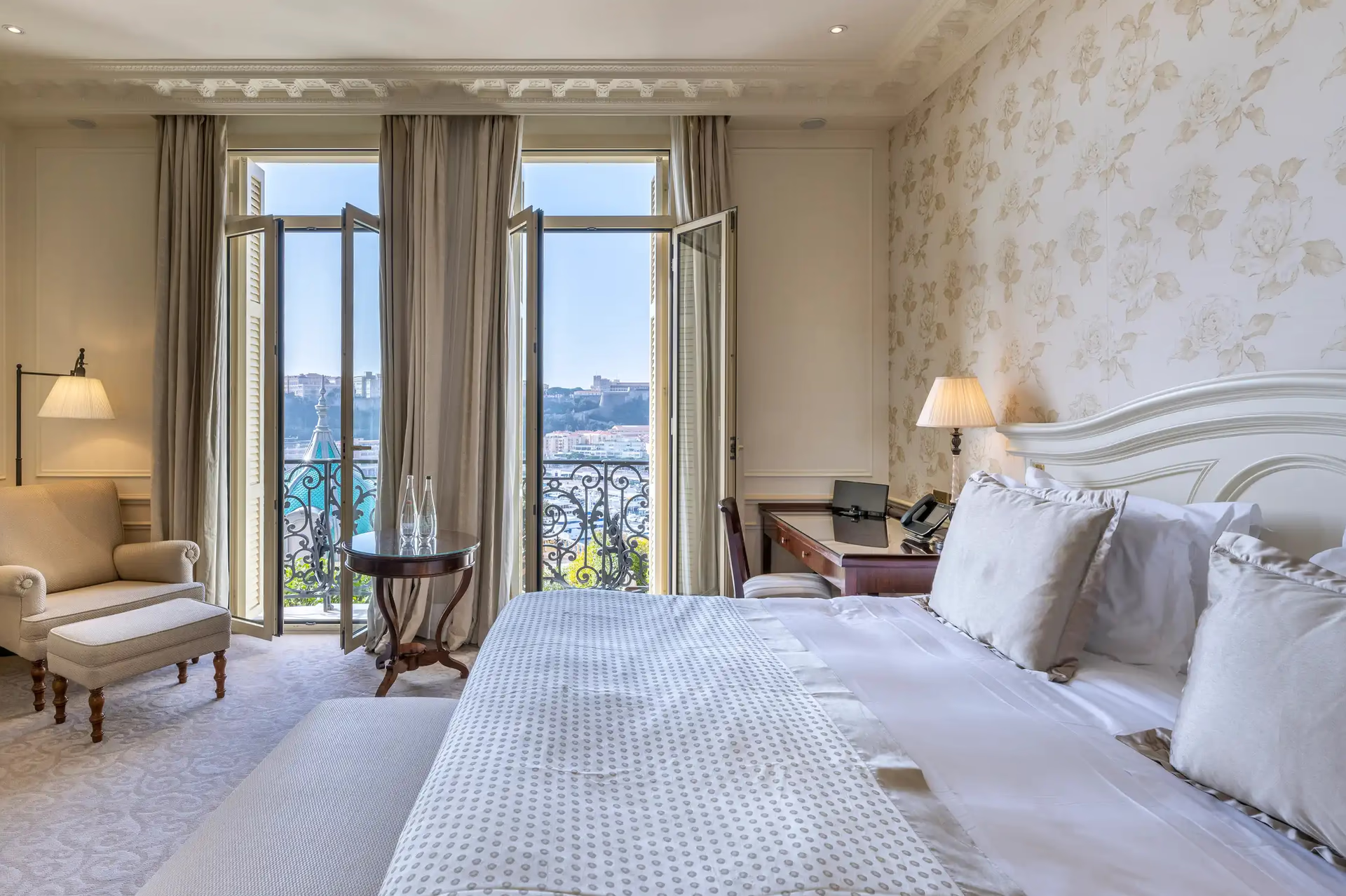 Suite bedroom with sea views through double doors, white bed and neutral furnishings