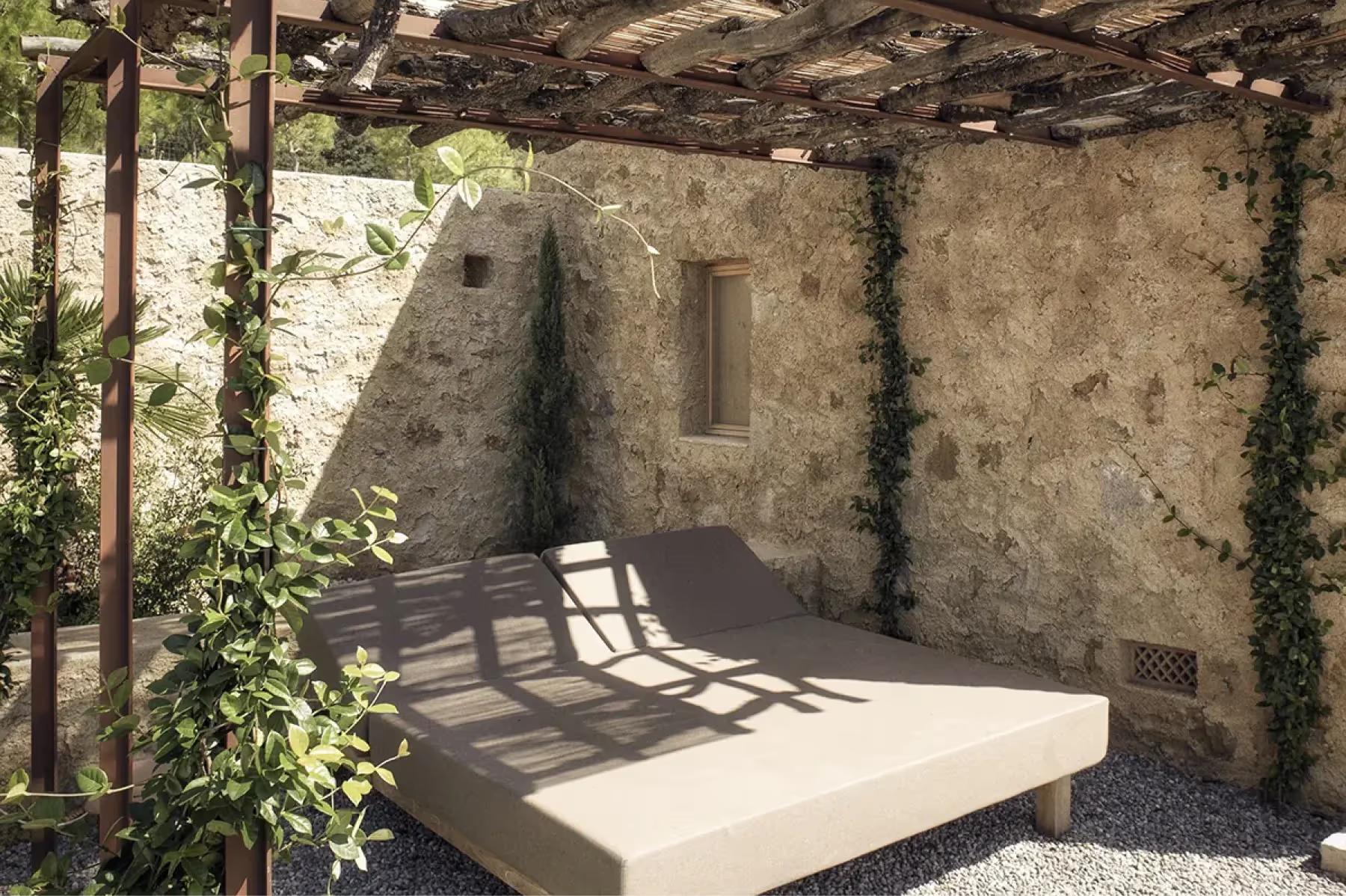 Es Racó d’Artà: sheltered outdoor sitting area beneath timber pergola with stone walls and natural vegetation